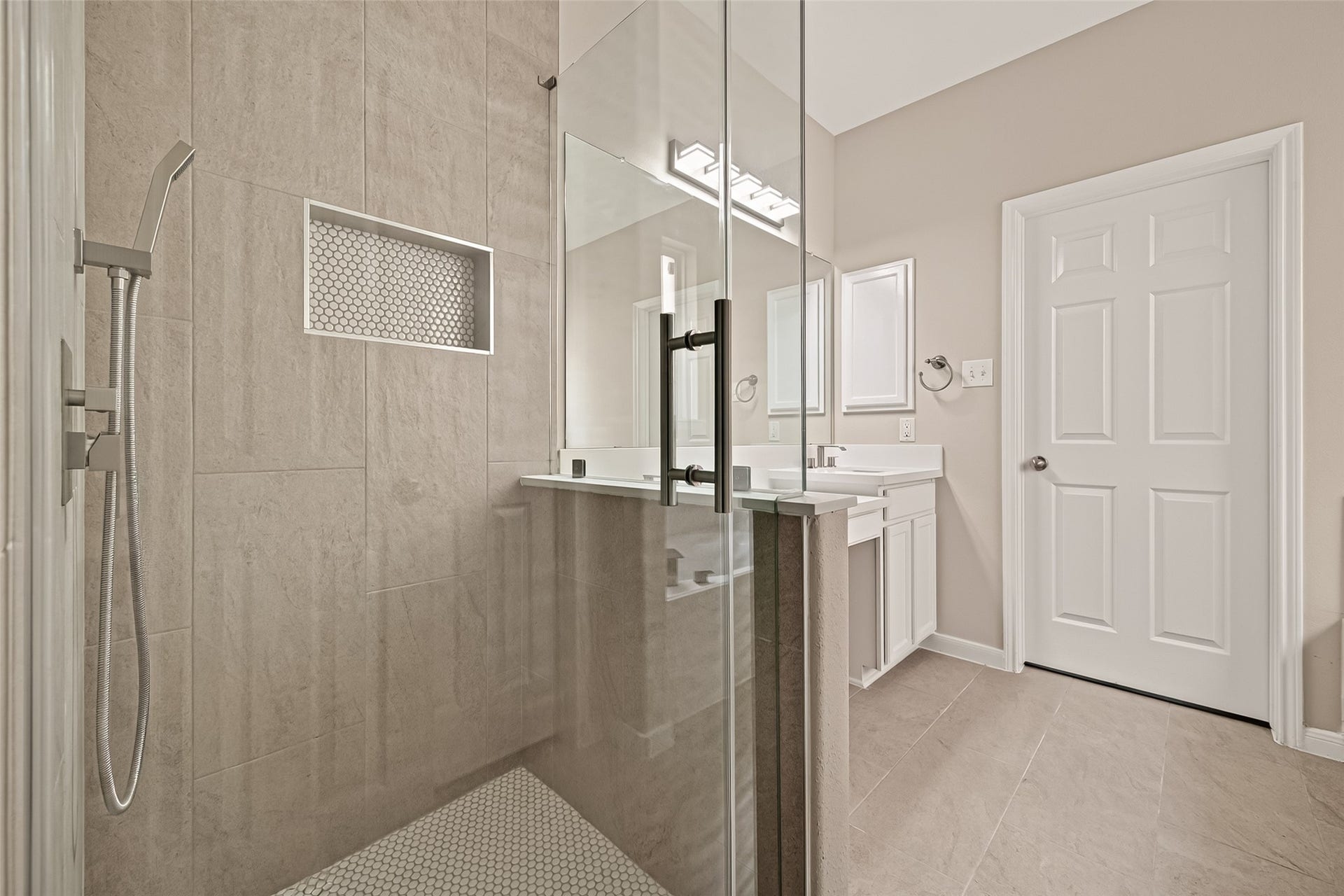 3635 Cottage Manor Lane, Katy, TX 77494 Walk-in shower with floor-to-ceiling tile, a penny-tile floor and niche, handheld showerhead, and a frameless glass enclosure.