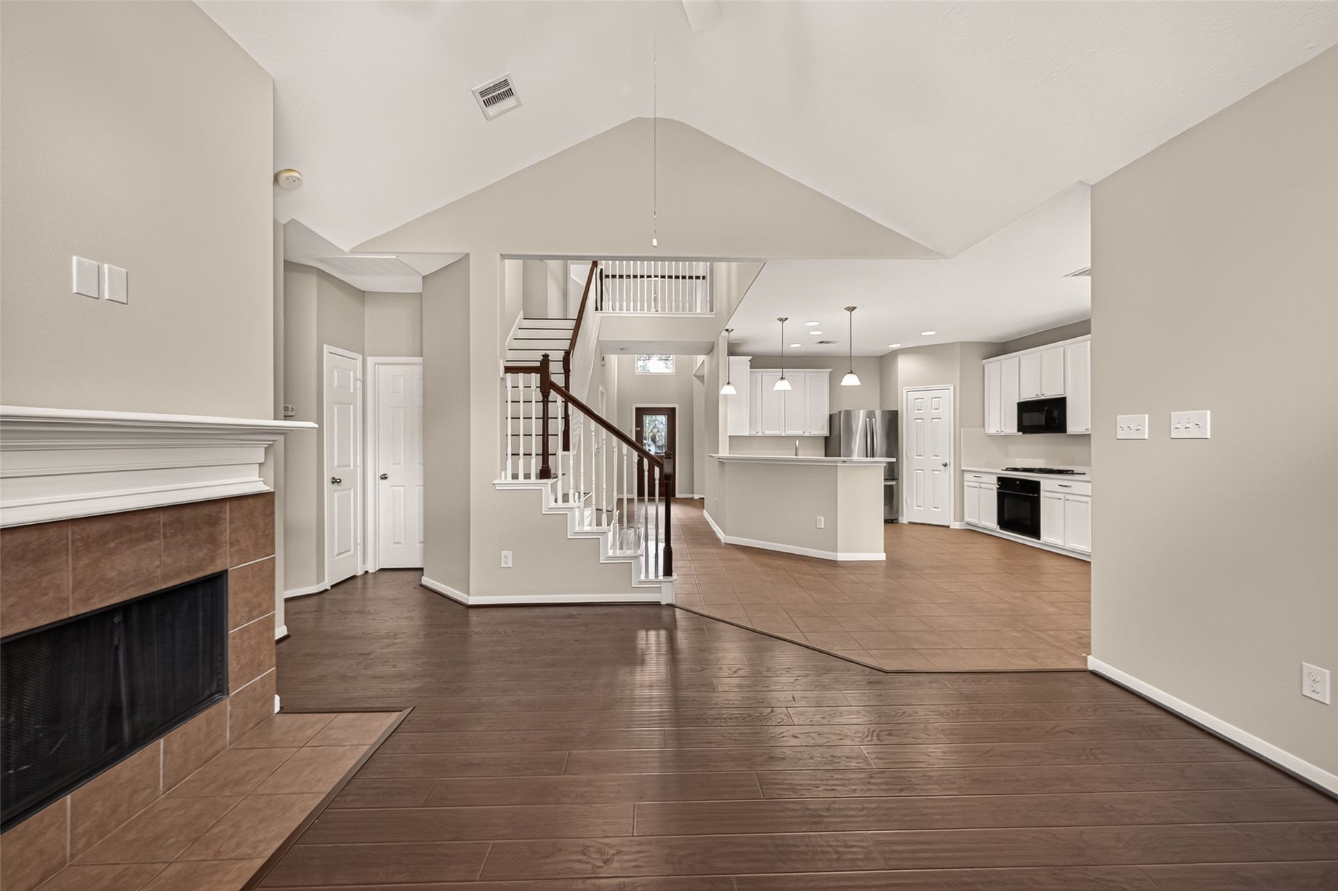 3635 Cottage Manor Lane, Katy, TX 77494 Vaulted ceilings and a fireplace with a classic white mantel highlight the living room. Rich wood-look flooring and an open connection to the kitchen create an inviting gathering space, with the staircase adding architectural character.