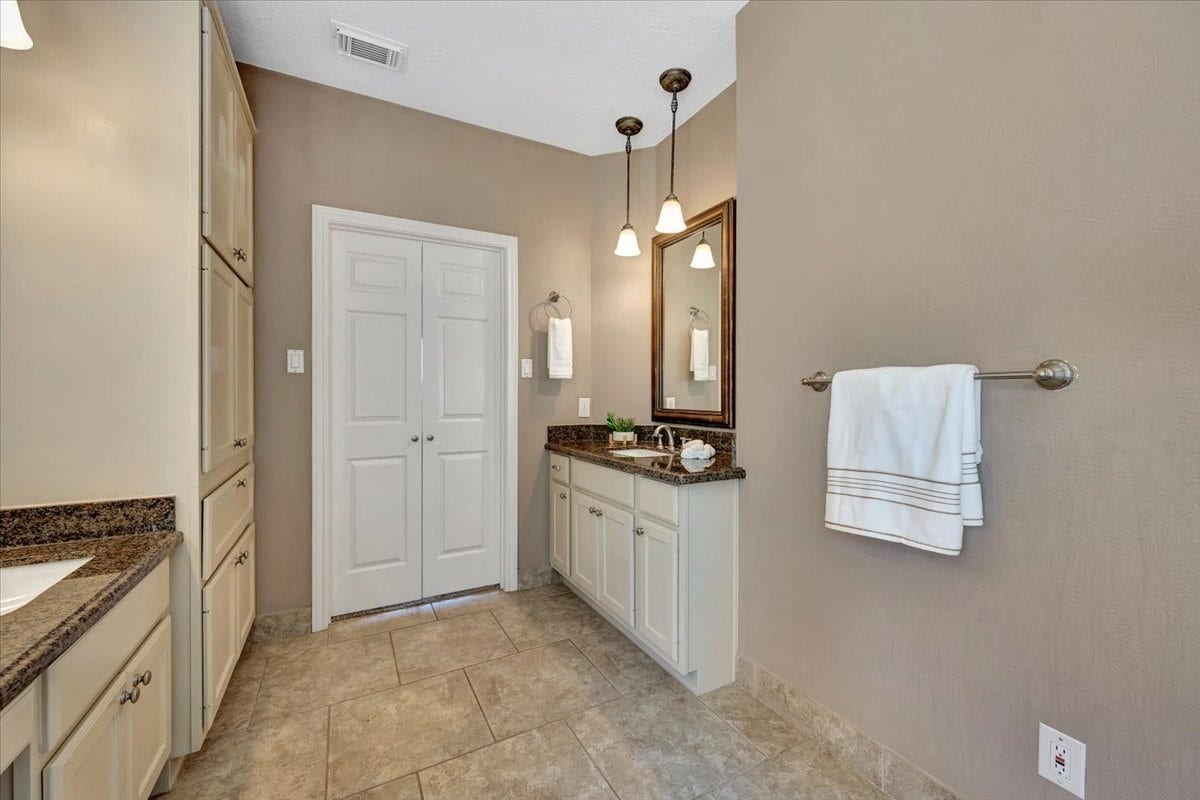 Primary suite featuring two vanities with sinks, sitting area, freestanding tub, separate glass-enclosed shower, expansive walk-in closet, and a private enclosed water closet.