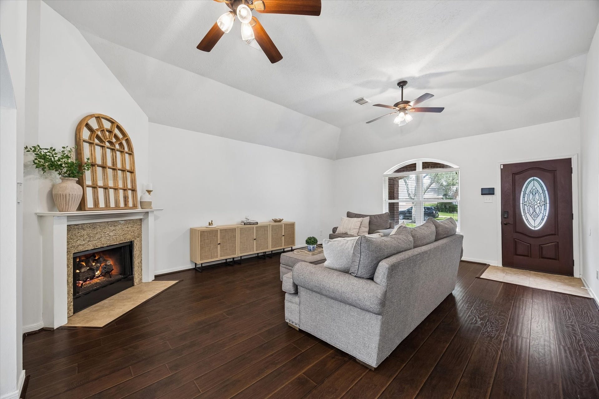 Light-filled living room with vaulted ceiling, fireplace and warm wood-look flooring.