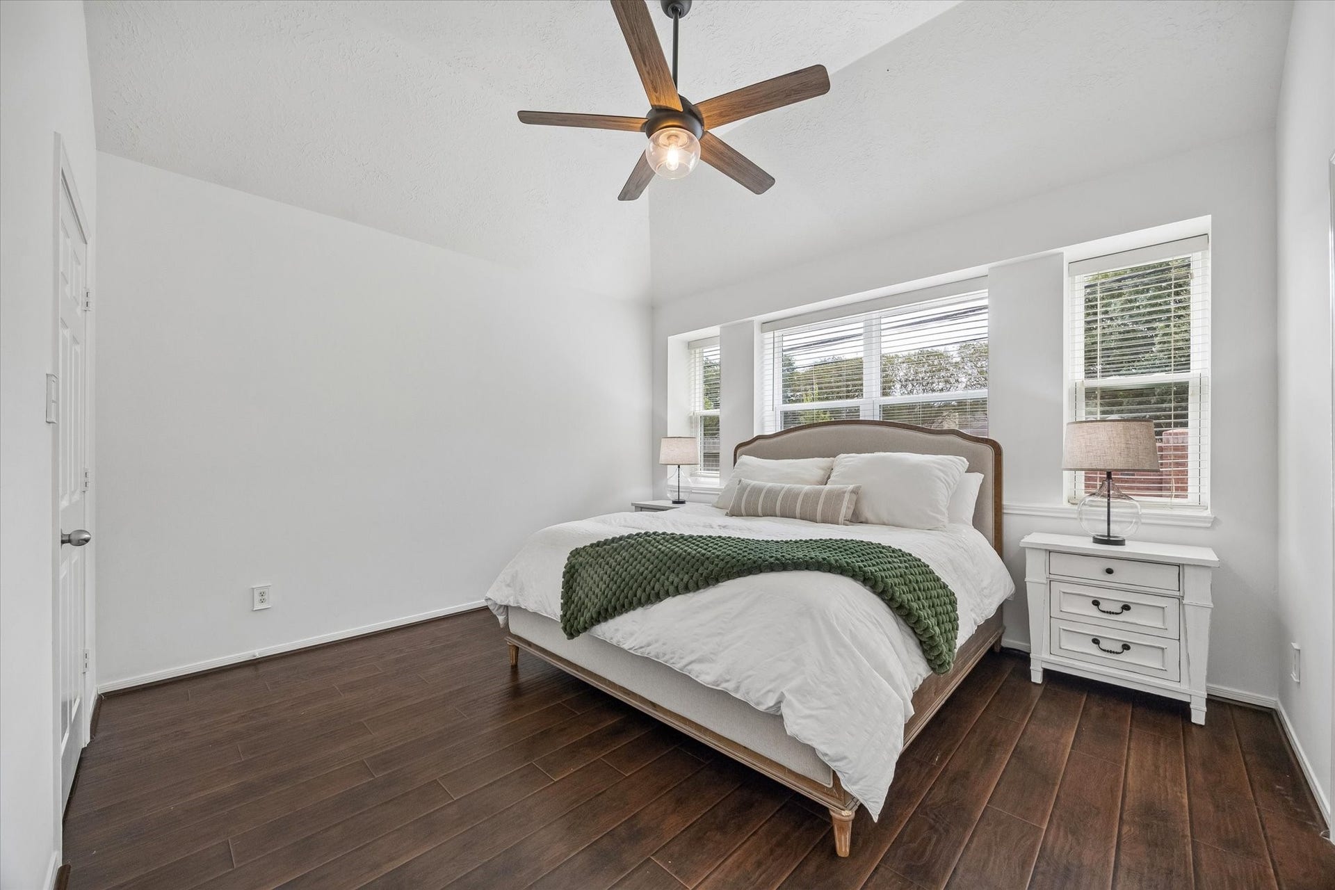 Second view of the primary bedroom highlights the vaulted ceiling, new windows and warm wood-look flooring.