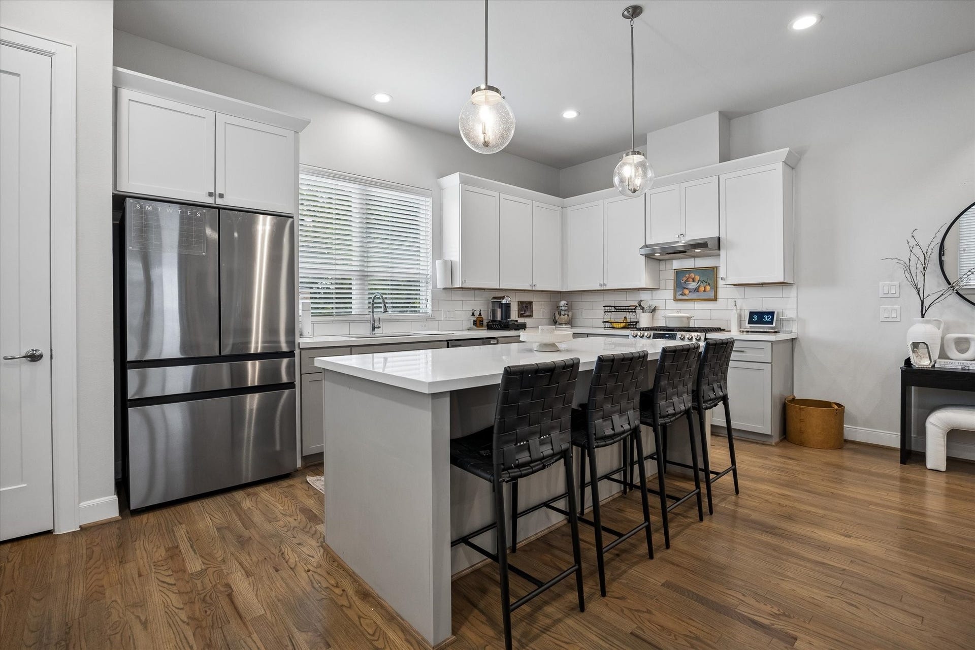 2491 W 11th Street, Houston, TX 77008 Another view of the kitchen highlights the oversized island with seating for four and ample workspace. Pendant lighting, white cabinetry, and stainless steel appliances complete the space.