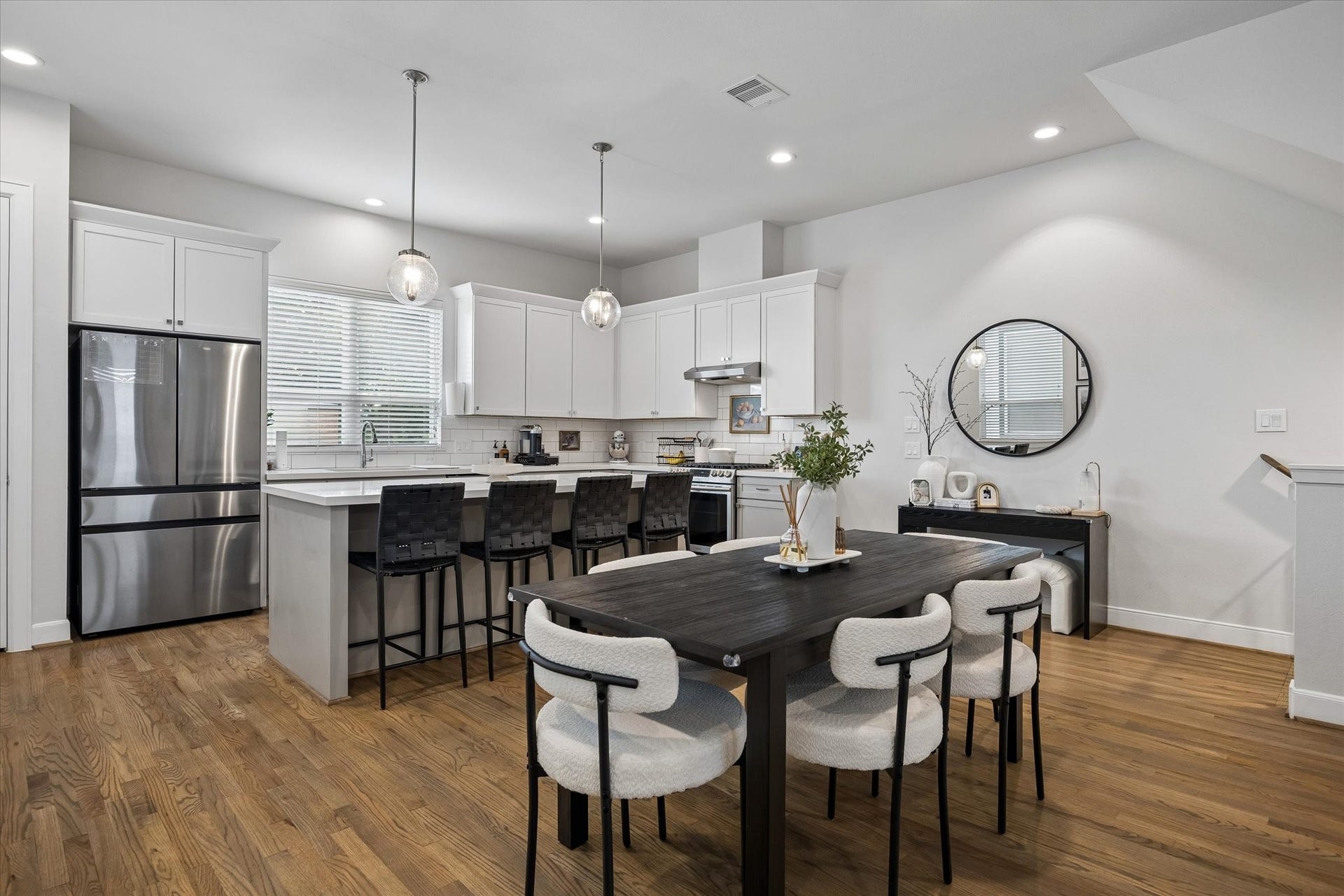 2491 W 11th Street, Houston, TX 77008 Open kitchen overlooks the dining area and offers a large island with additional seating. White cabinetry, stainless steel appliances, and hardwood flooring create a timeless, neutral aesthetic.