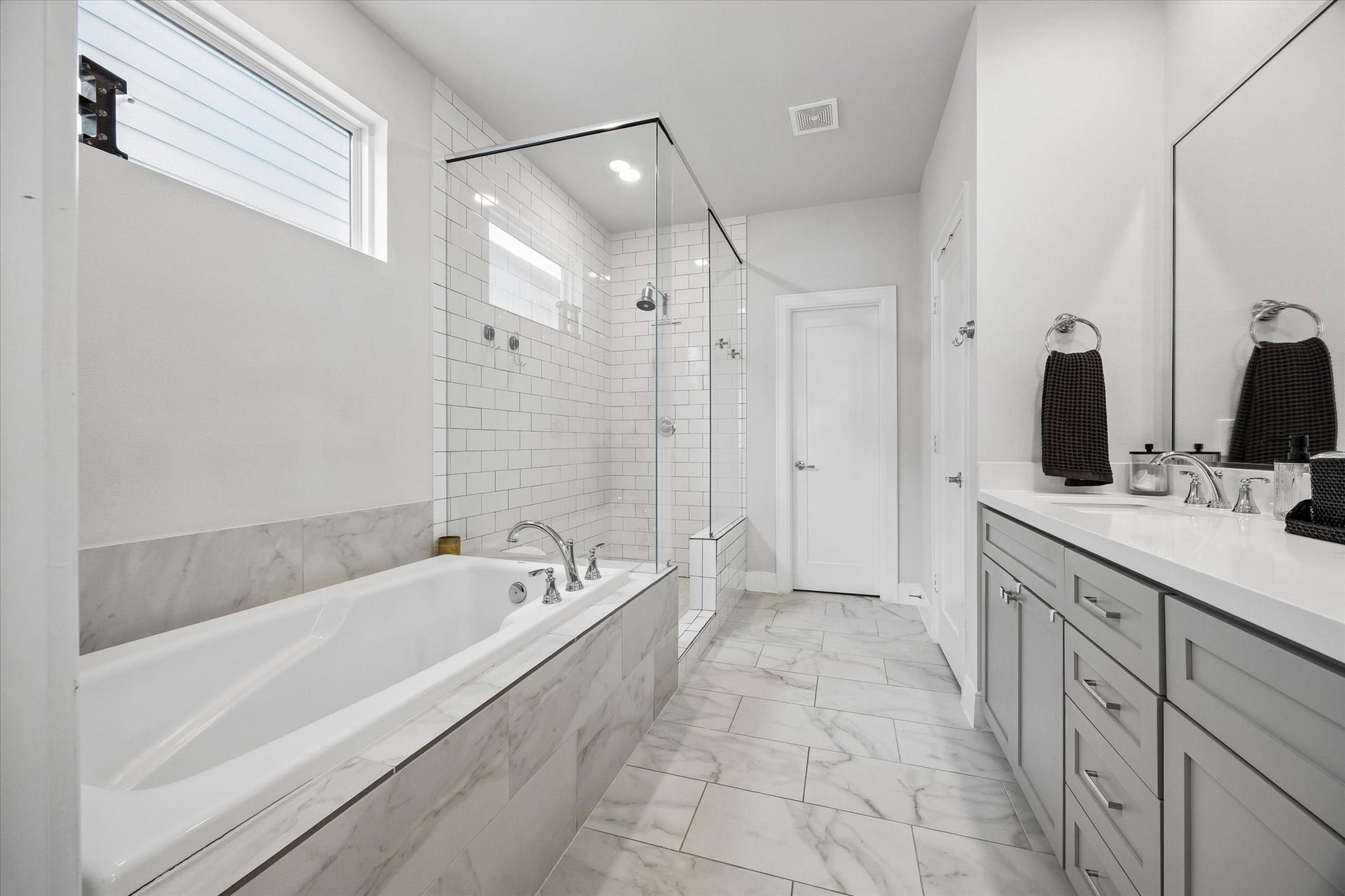 2491 W 11th Street, Houston, TX 77008 Primary bath includes a separate soaking tub with marble-look surround and a nearby walk-in shower. A high window brings natural light into the space while maintaining privacy.