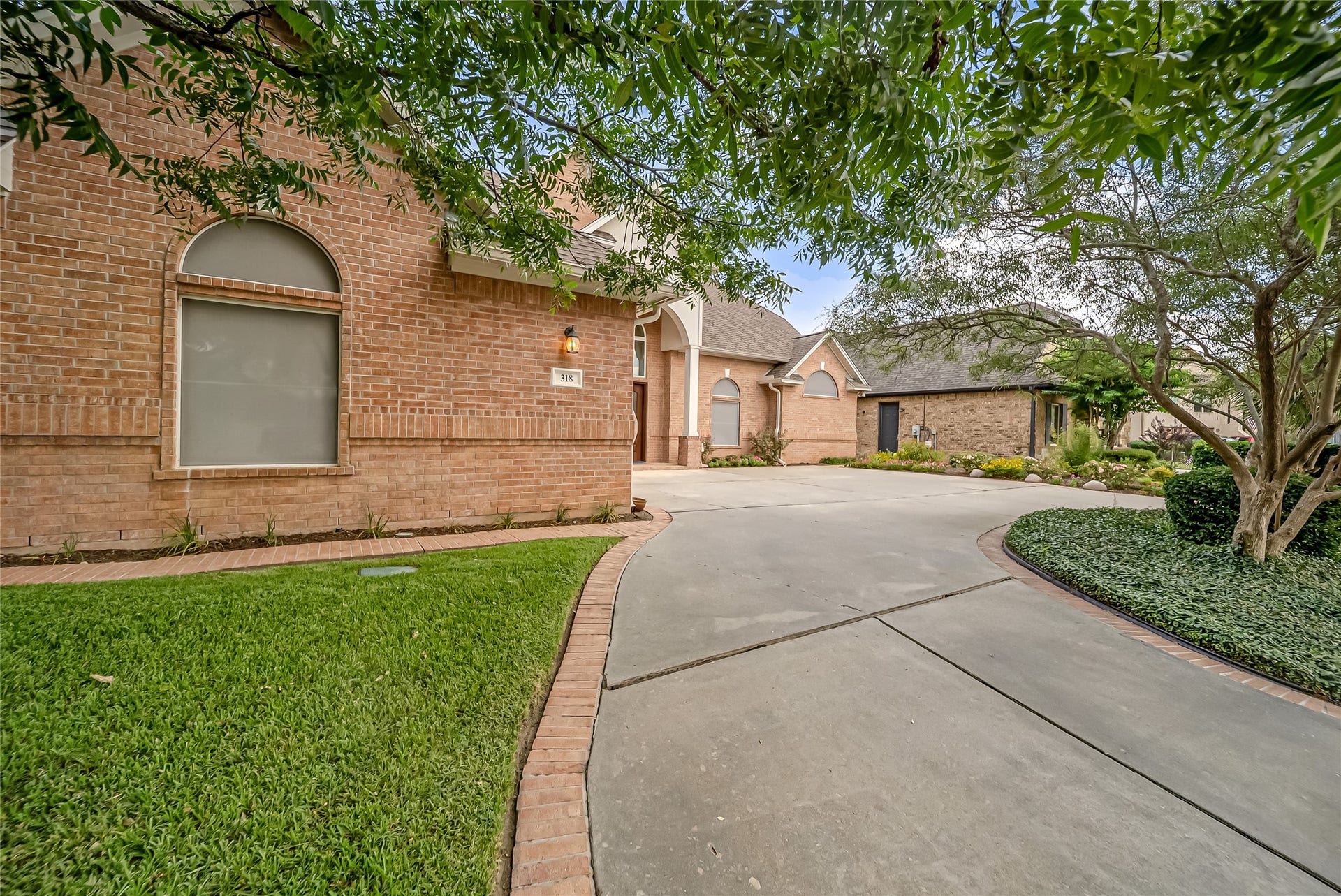 318 Bayshore Drive, Montgomery, TX 77356 Lush landscaping, mature trees, and an expansive curved driveway enhance the home's elegant exterior, creating a private and inviting entrance to this beautifully maintained waterfront retreat.