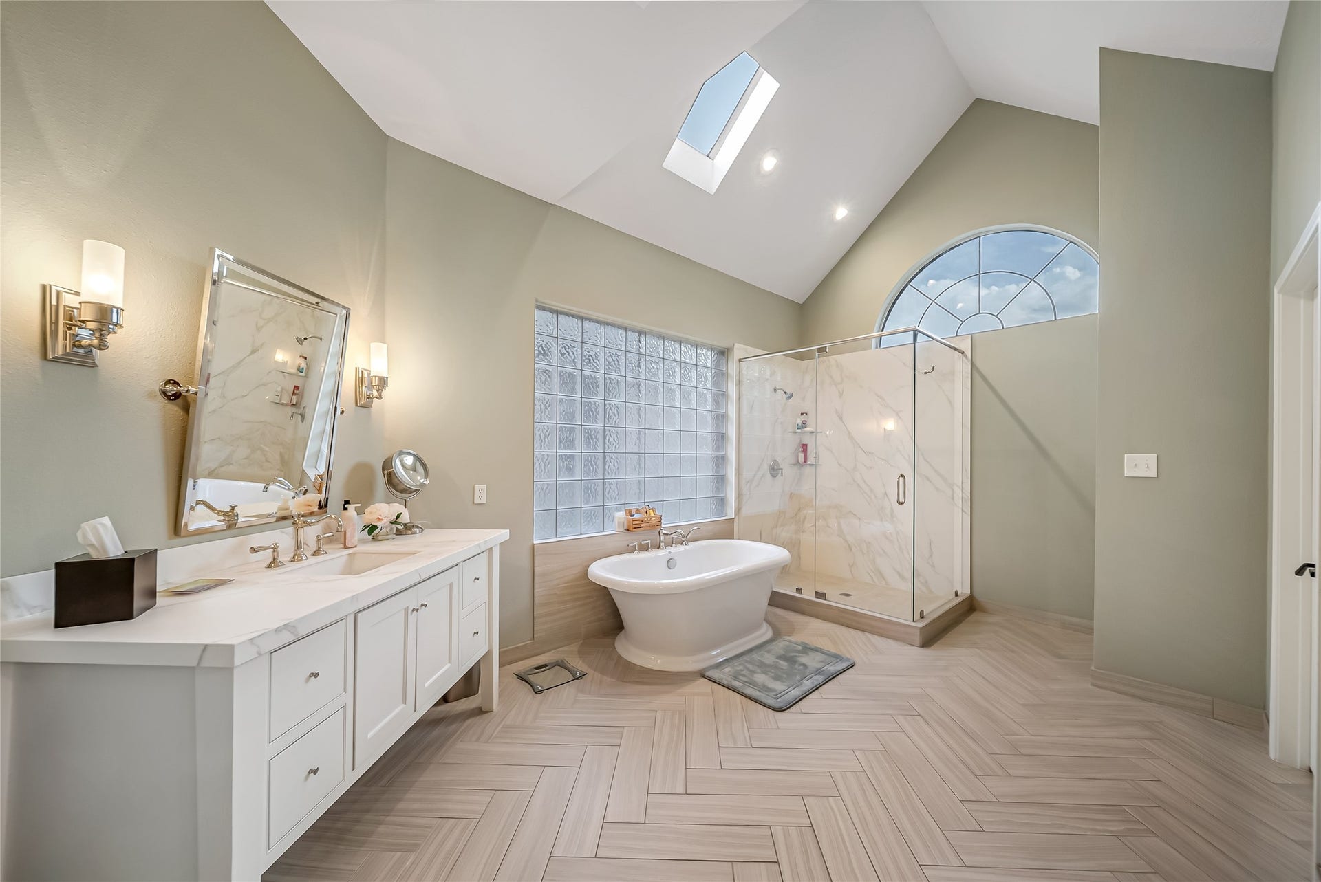 318 Bayshore Drive, Montgomery, TX 77356 Thoughtfully redesigned with timeless elegance, the primary ensuite features exquisite herringbone wood-look tile flooring, a freestanding soaking tub, an oversized walk-in shower, and vaulted ceilings illuminated by a skylight, creating a true spa-like sanctuary.