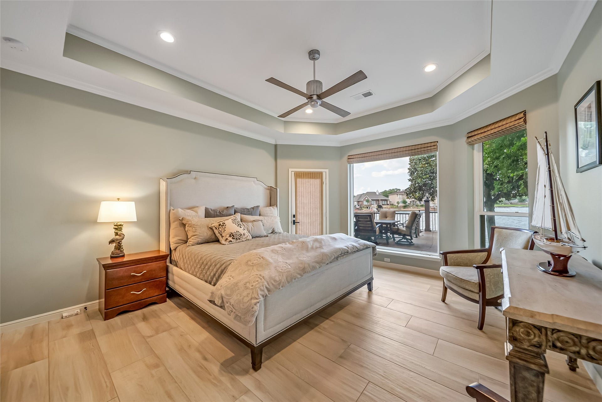 318 Bayshore Drive, Montgomery, TX 77356 Elegantly appointed with a tray ceiling and continuous wood-grain tile flooring, the first-floor primary suite embraces its waterfront setting through expansive windows overlooking the lake and private access to the covered patio, creating a peaceful retreat.