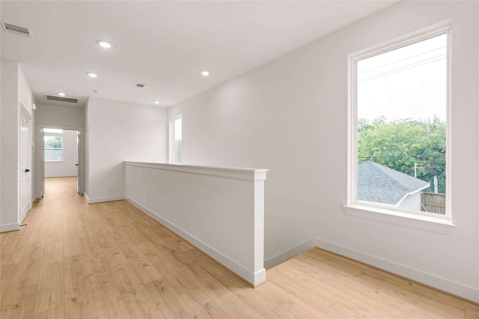 5016 Schuler Street, Houston, TX 77007 Upper-level landing bright picture window framing tree-lined views, half-wall partition, and wide-plank wood-look flooring throughout.