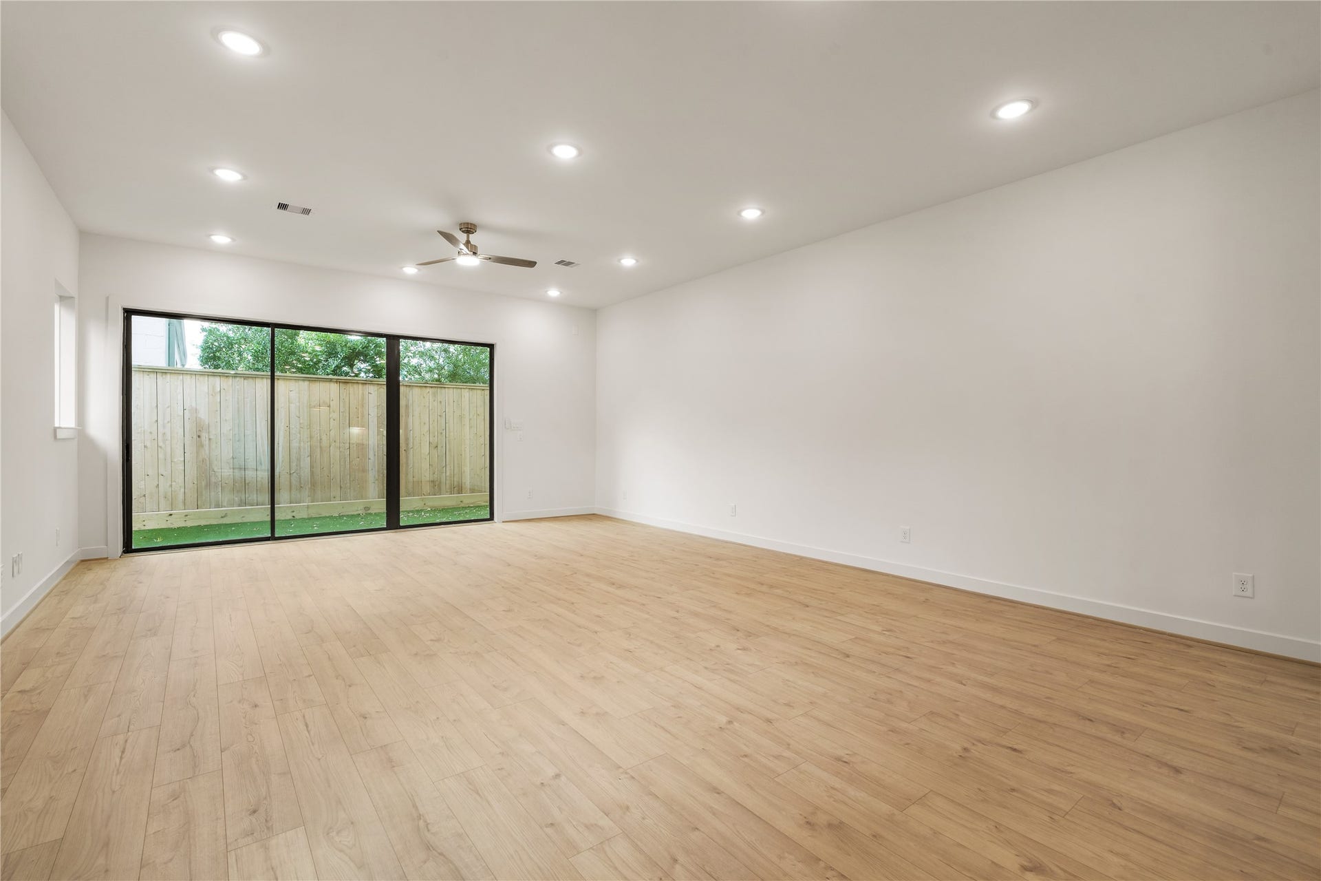 5016 Schuler Street, Houston, TX 77007 Sunlit living retreat floor-to-ceiling multi-slide glass doors opening directly to the private yard, framed by warm wood flooring and recessed LED lighting.