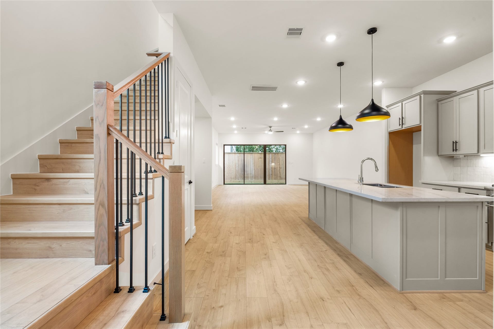 5016 Schuler Street, Houston, TX 77007 Grand main-level floor plan expansive quartz kitchen island, matte black dome pendant lights, custom wood-and-iron staircase, and floor-to-ceiling glass patio doors.