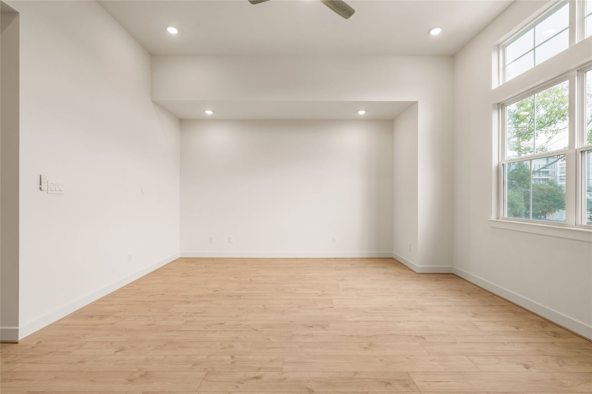 5016 Schuler Street, Houston, TX 77007 Sun-drenched primary suite oversized window bringing in leafy outdoor views, soaring ceilings, and warm wood flooring throughout.