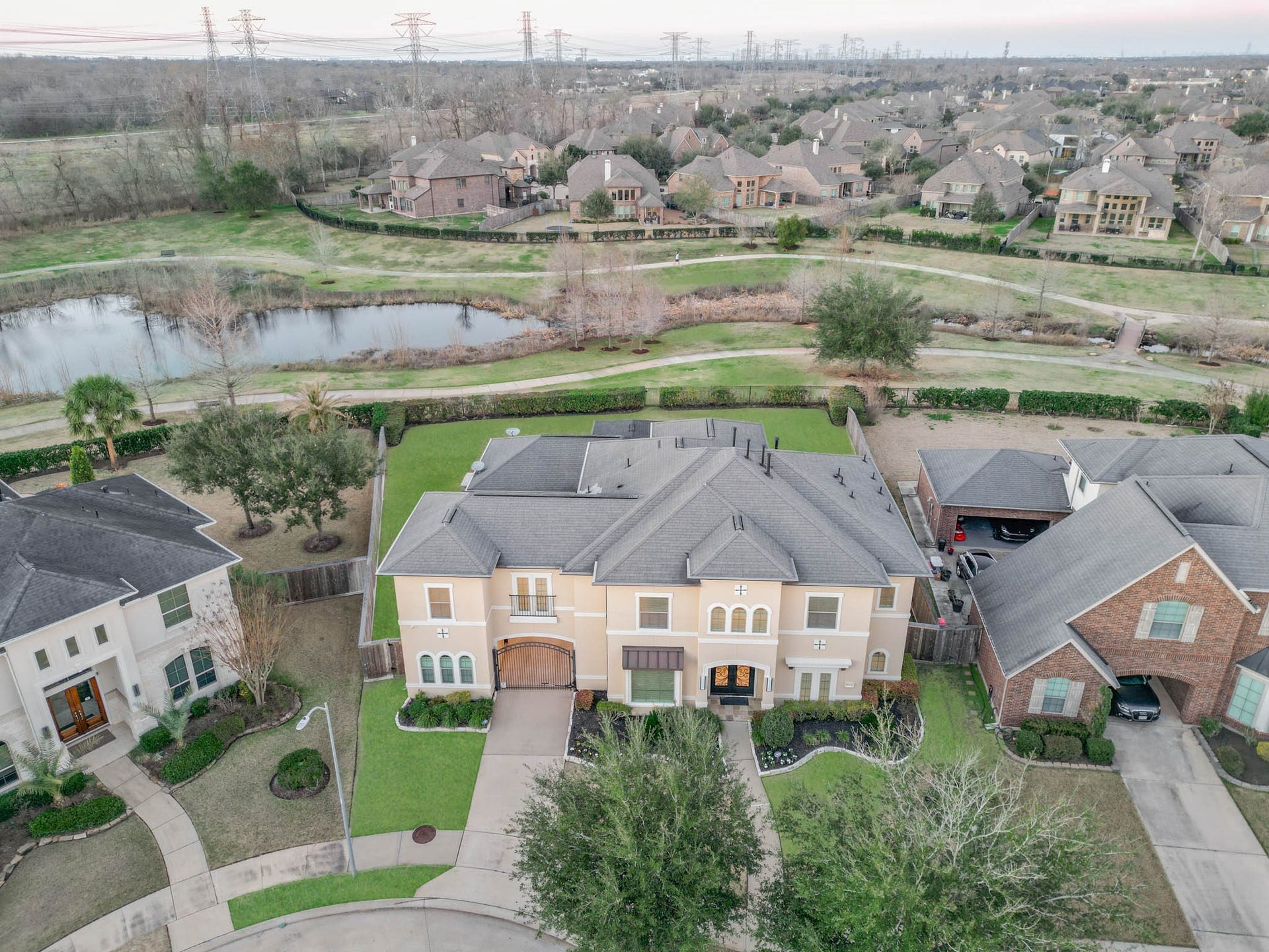 This aerial photo showcases a spacious, elegant home in a suburban neighborhood. The property features is situated near on a walking trails, providing a peaceful, scenic backdrop. The surrounding area includes other attractive homes and lush greenery, ideal for families seeking a tranquil setting. It is a few minutes walk to Anne Sullivan Elementary