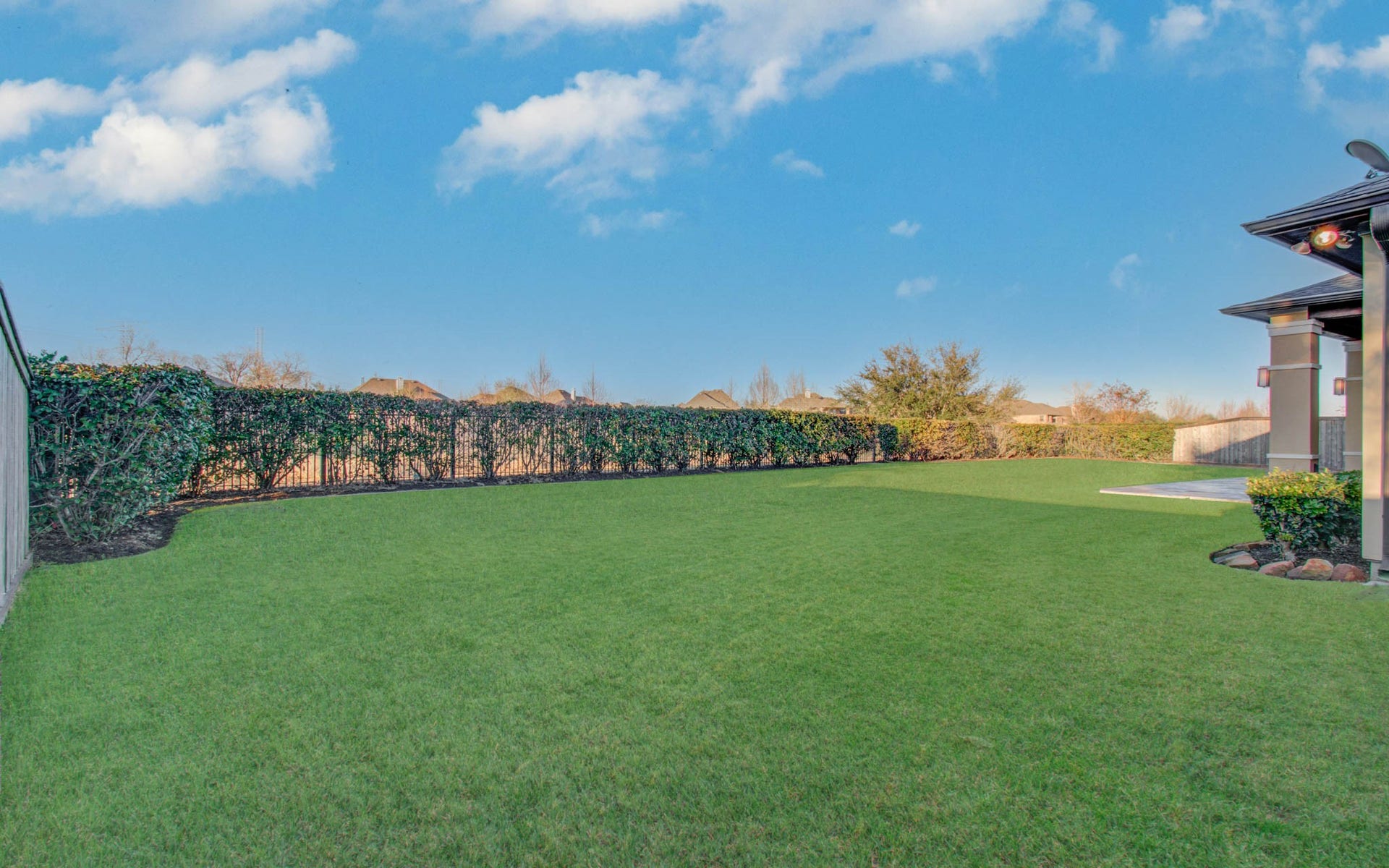 Spacious backyard with a well-maintained lawn, privacy hedges, and a covered patio area perfect for outdoor relaxation.