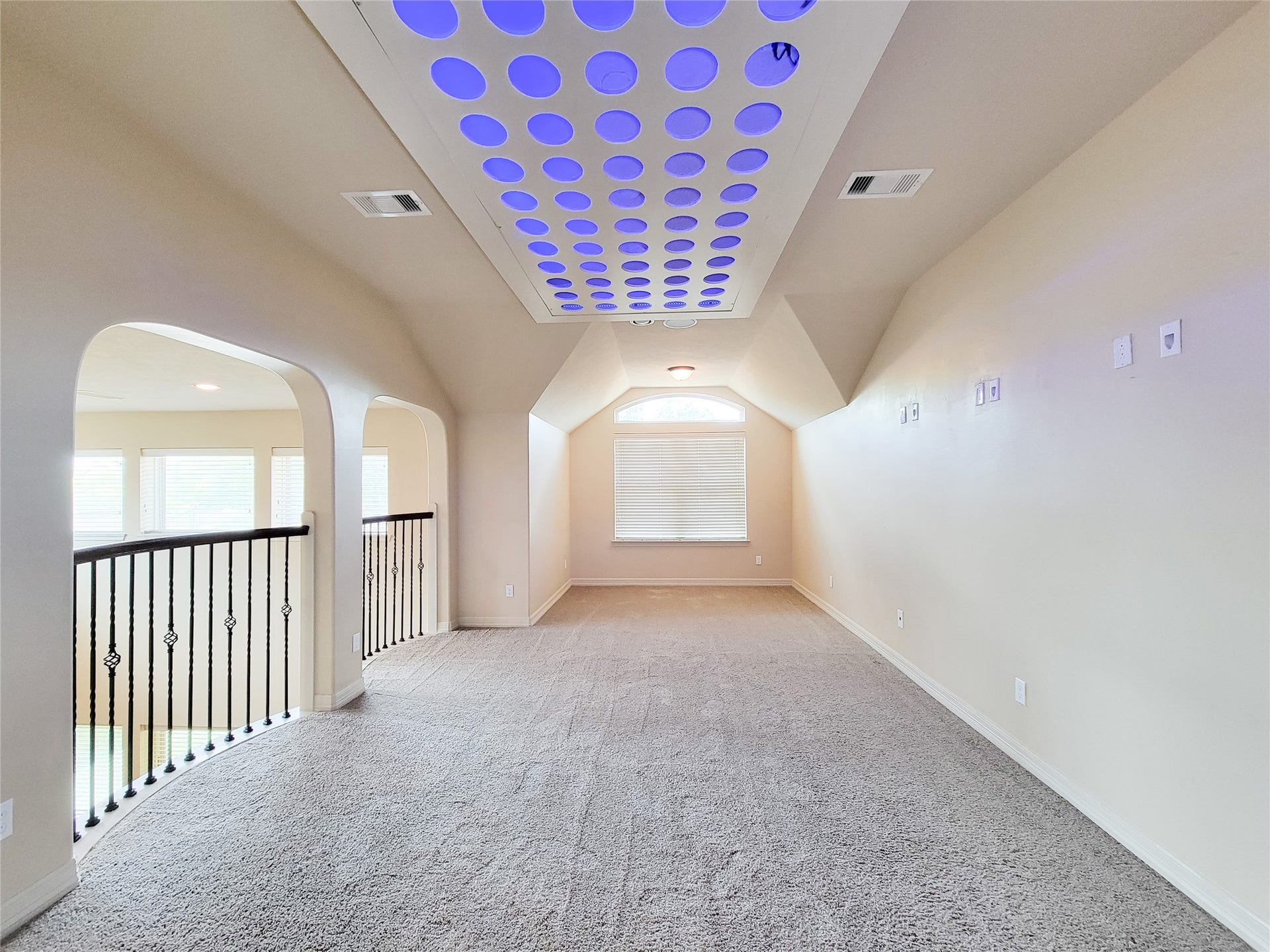 2210 Pearl Bay Court, Pearland, TX 77584 This spacious room features vaulted ceilings with unique circular lighting, carpeted floors, and a large window for natural light. It's adjacent to a railing overlooking the lower floor, adding an open, airy feel.