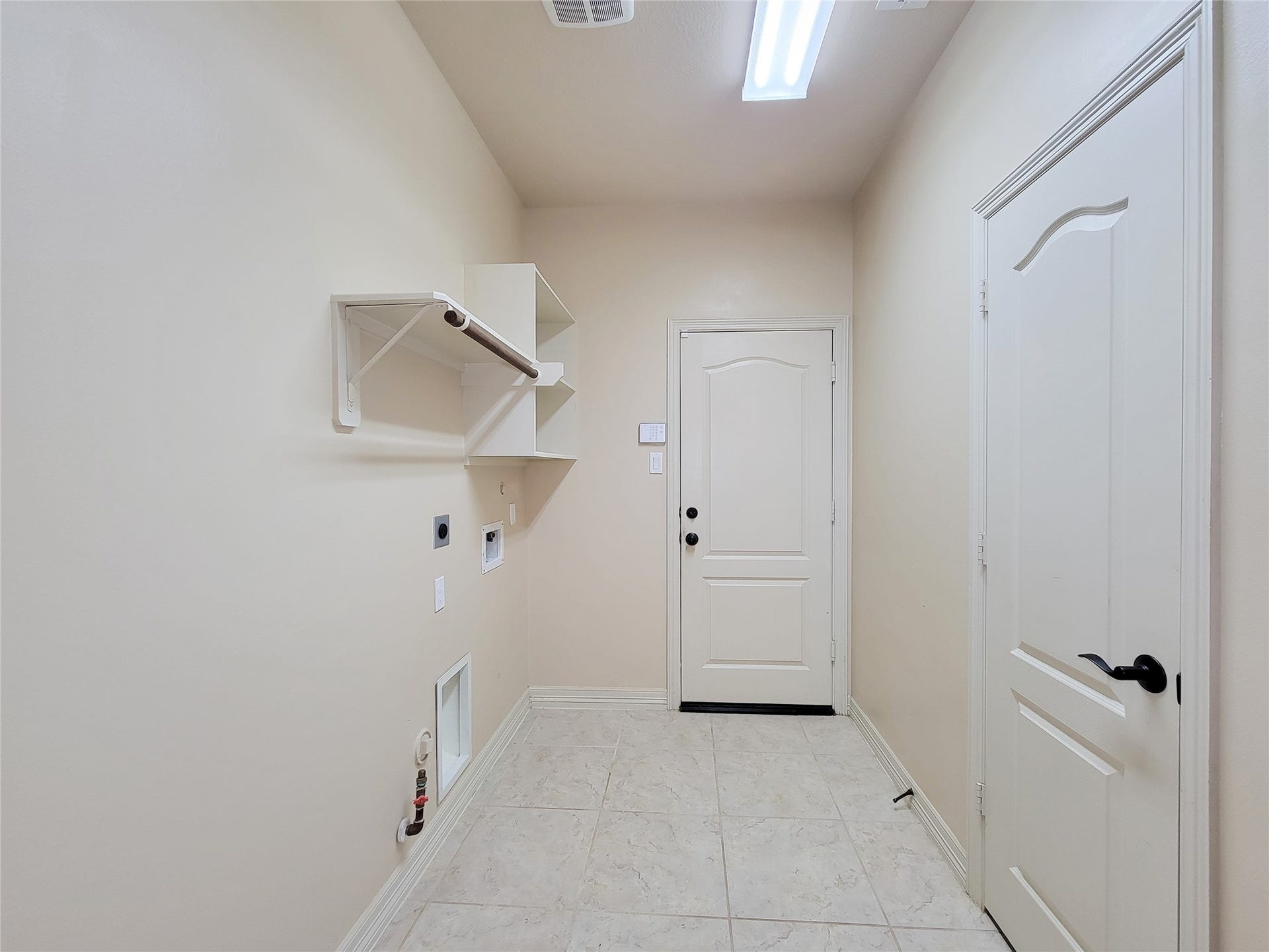 2210 Pearl Bay Court, Pearland, TX 77584 This is a bright and spacious laundry room with tiled flooring, built-in shelving, and connections for appliances. It features two doors, likely leading to additional storage or utility areas.