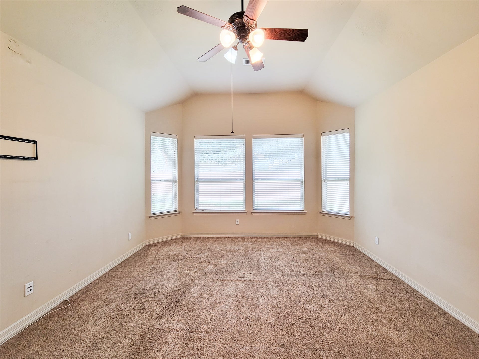 2210 Pearl Bay Court, Pearland, TX 77584 Spacious room with a high ceiling and neutral walls, featuring a central ceiling fan and multiple large windows for ample natural light. The carpeted floor adds warmth and comfort.