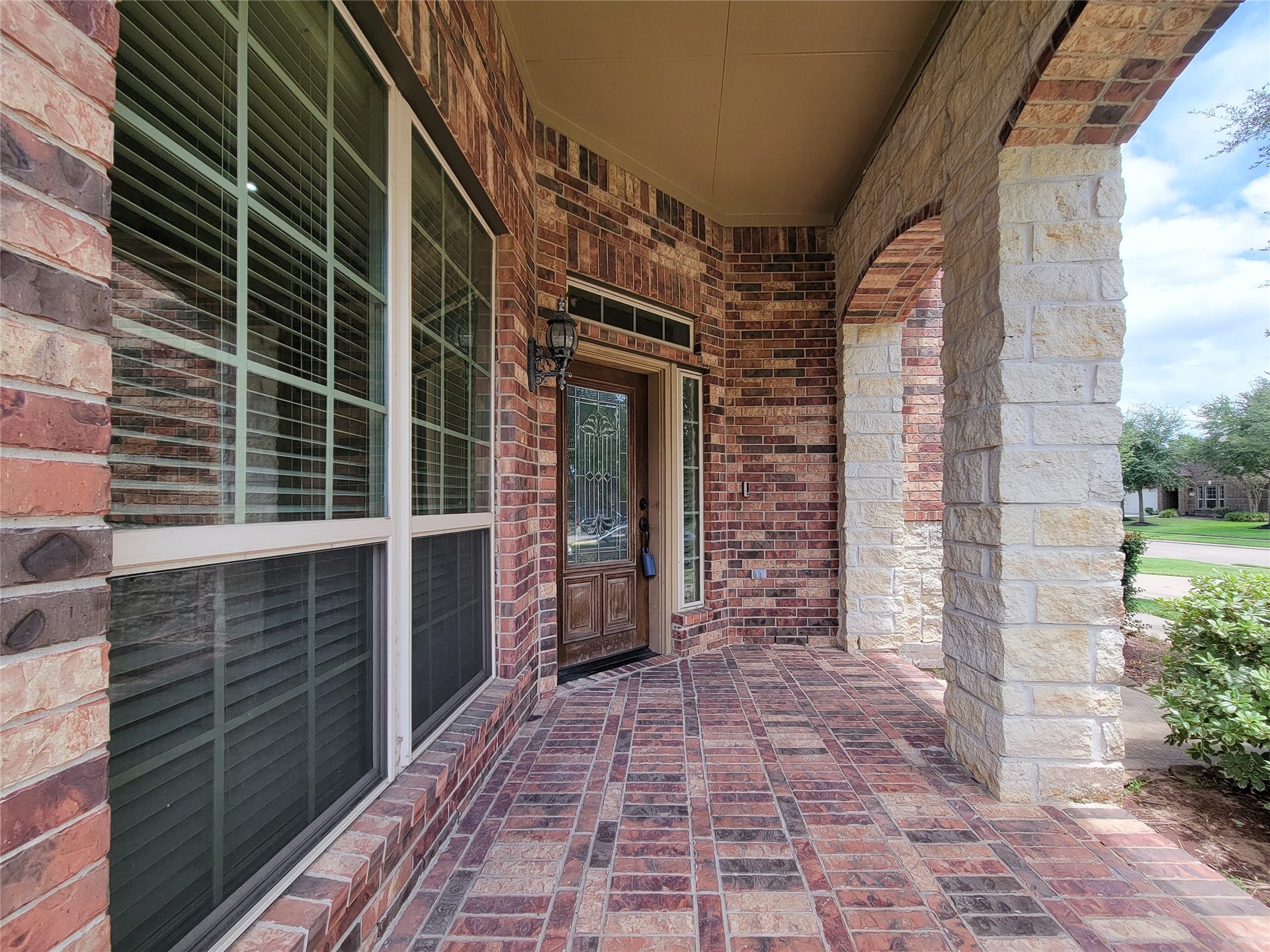 2210 Pearl Bay Court, Pearland, TX 77584 This photo showcases a welcoming front porch with a brick and stone facade. It features a beautiful wooden door with decorative glass, large windows with shutters, and a covered entryway that adds charm and protection from the elements. The porch is spacious, offering potential for outdoor seating or decor.