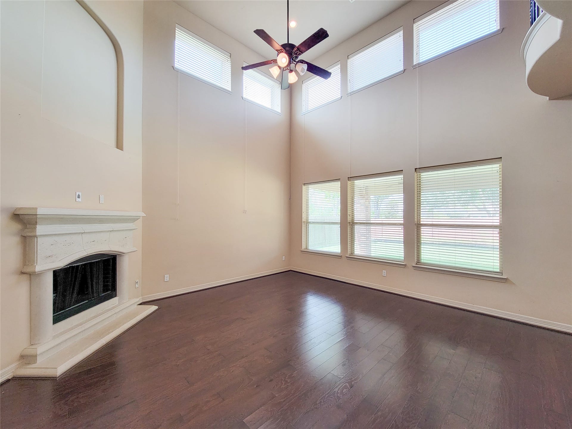 2210 Pearl Bay Court, Pearland, TX 77584 This spacious living room features high ceilings, large windows for ample natural light, a ceiling fan, and a cozy fireplace, all complemented by elegant hardwood floors.