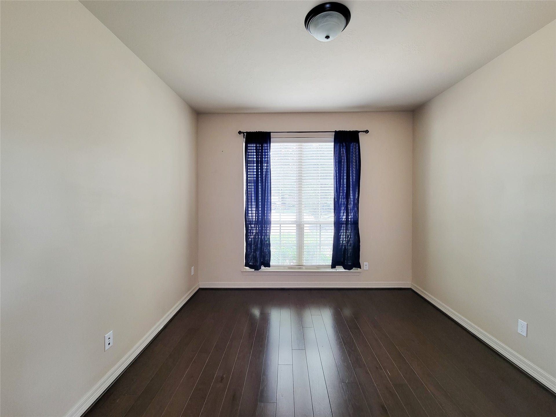 2210 Pearl Bay Court, Pearland, TX 77584 This room features dark hardwood flooring and neutral walls, with a large window dressed in sheer blue curtains, allowing natural light to filter through.