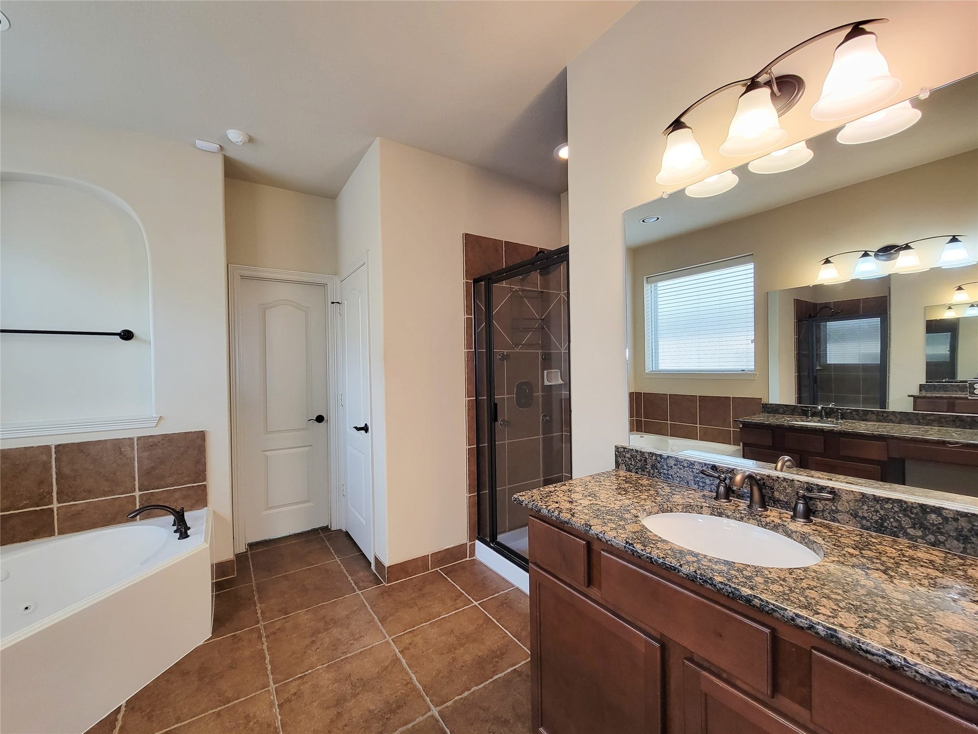2210 Pearl Bay Court, Pearland, TX 77584 Spacious bathroom with a granite countertop, double vanity, and elegant lighting. Features a large tub, separate glass-enclosed shower, and neutral tile flooring for a modern feel.