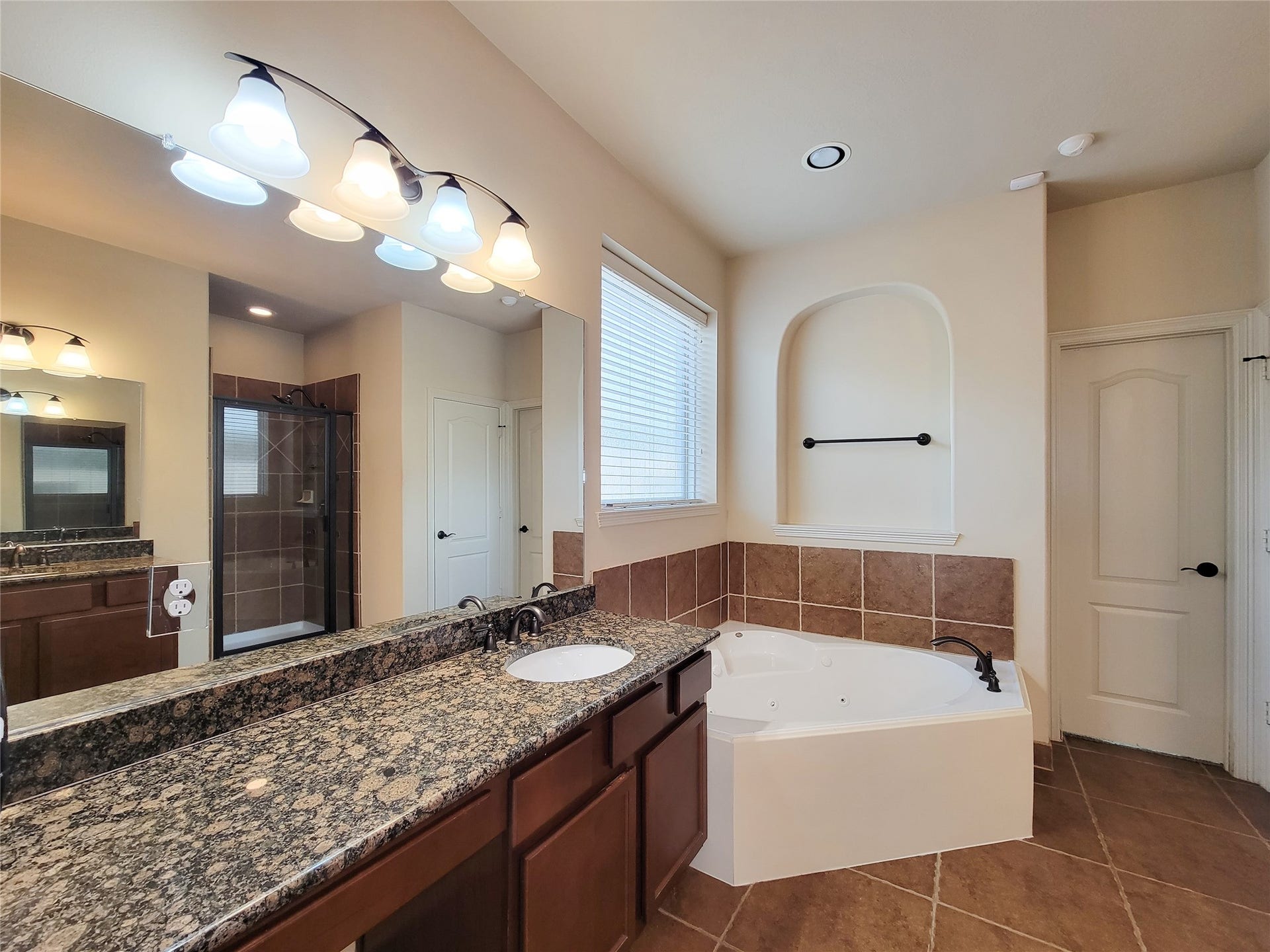2210 Pearl Bay Court, Pearland, TX 77584 This spacious bathroom features a dual-sink granite vanity, a corner soaking tub, and a separate walk-in shower. Warm tile flooring and modern lighting create a relaxing atmosphere.
