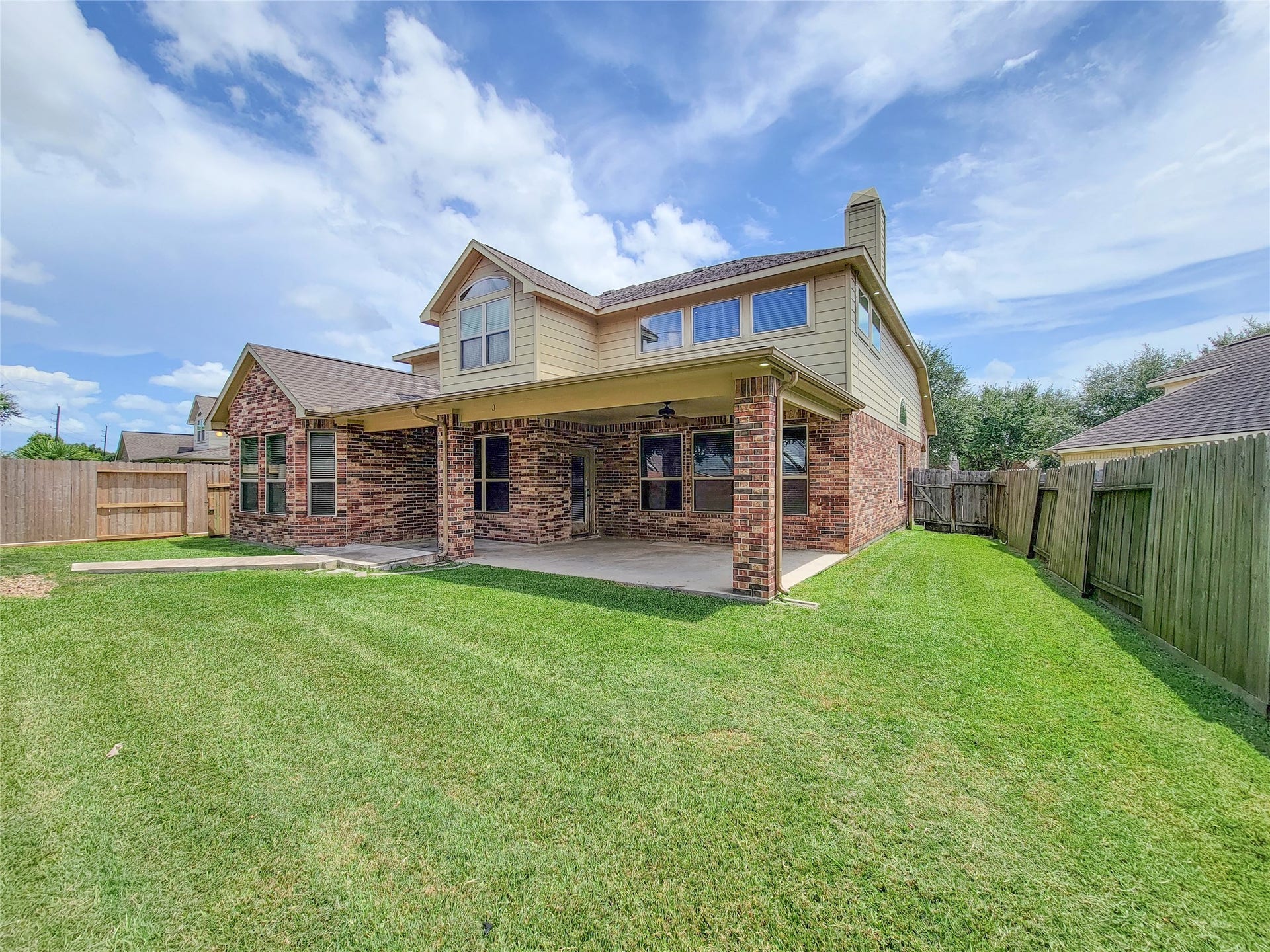 2210 Pearl Bay Court, Pearland, TX 77584 This photo showcases a spacious backyard with a well-maintained lawn, a covered patio, and a two-story brick house. The fenced yard offers privacy and the patio is perfect for outdoor gatherings.