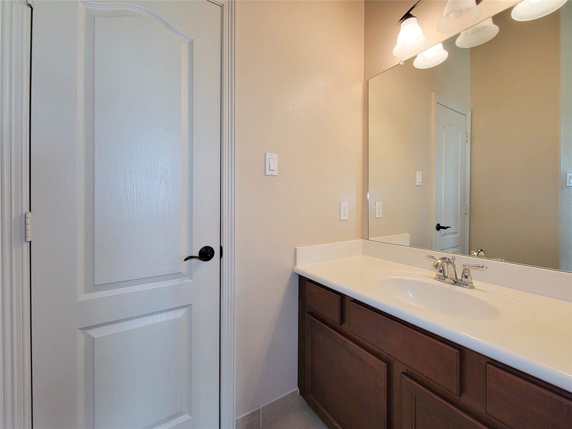 2210 Pearl Bay Court, Pearland, TX 77584 This bathroom features a single vanity with a sleek white countertop, warm wood cabinetry, and a large mirror. The neutral walls and classic light fixtures create a bright and inviting space.