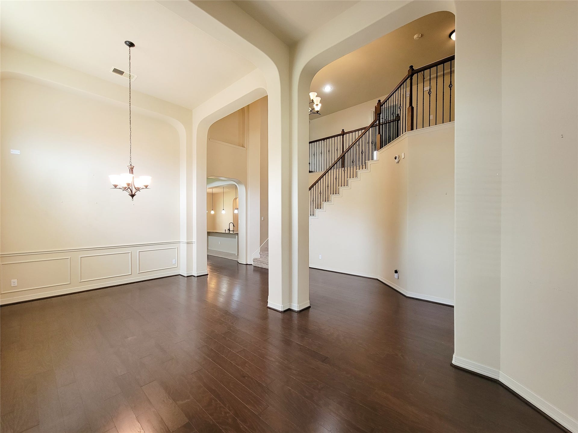 2210 Pearl Bay Court, Pearland, TX 77584 This inviting space features high ceilings, elegant archways, and dark hardwood floors. The open layout includes a dining area with a modern chandelier and an elegant staircase leading to the upper floor, offering a warm and spacious ambiance.