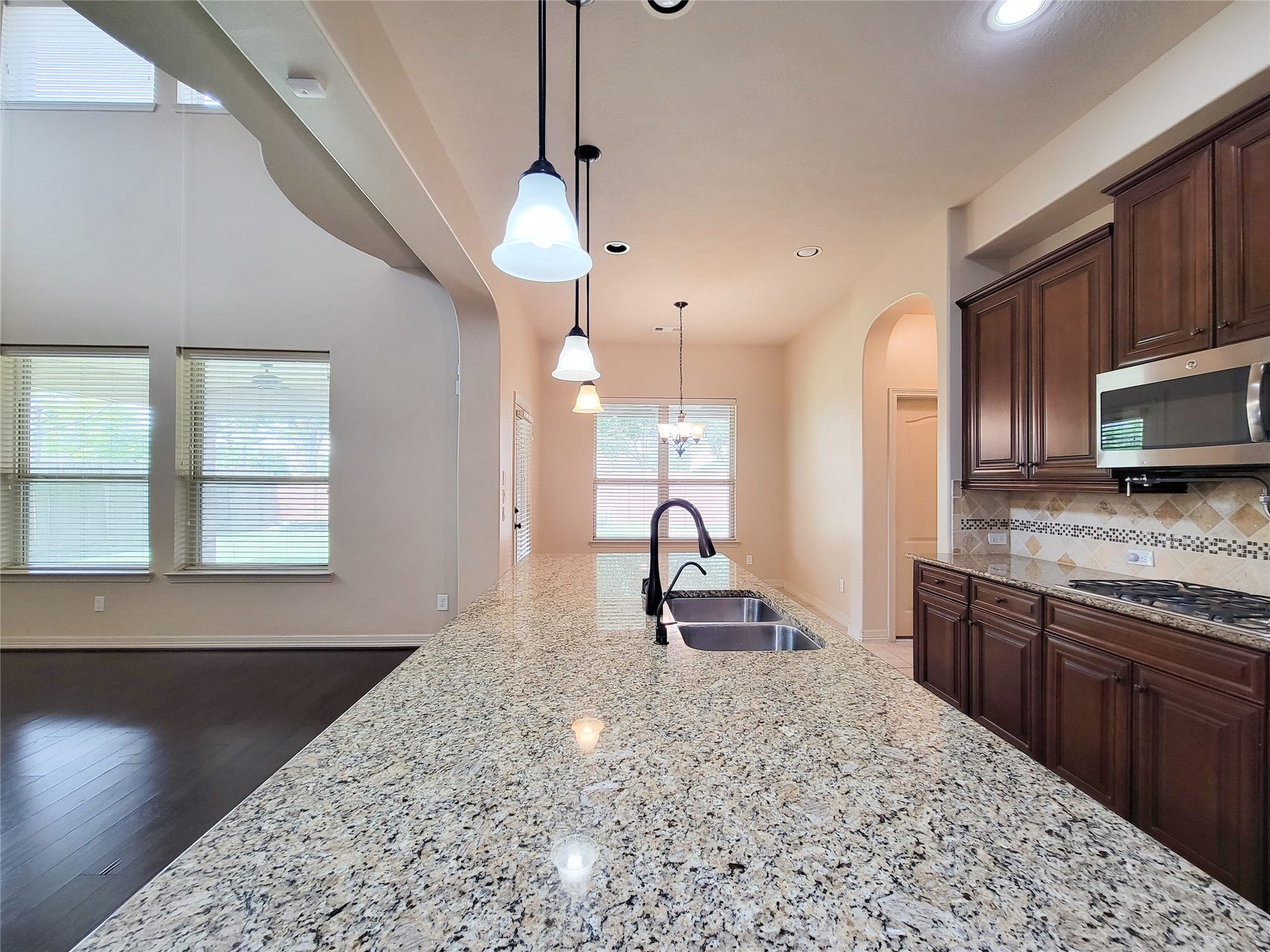 2210 Pearl Bay Court, Pearland, TX 77584 This kitchen features a spacious granite countertop with a built-in sink, dark wood cabinetry, and stainless steel appliances. The open layout includes large windows and pendant lighting, creating a bright and welcoming atmosphere.