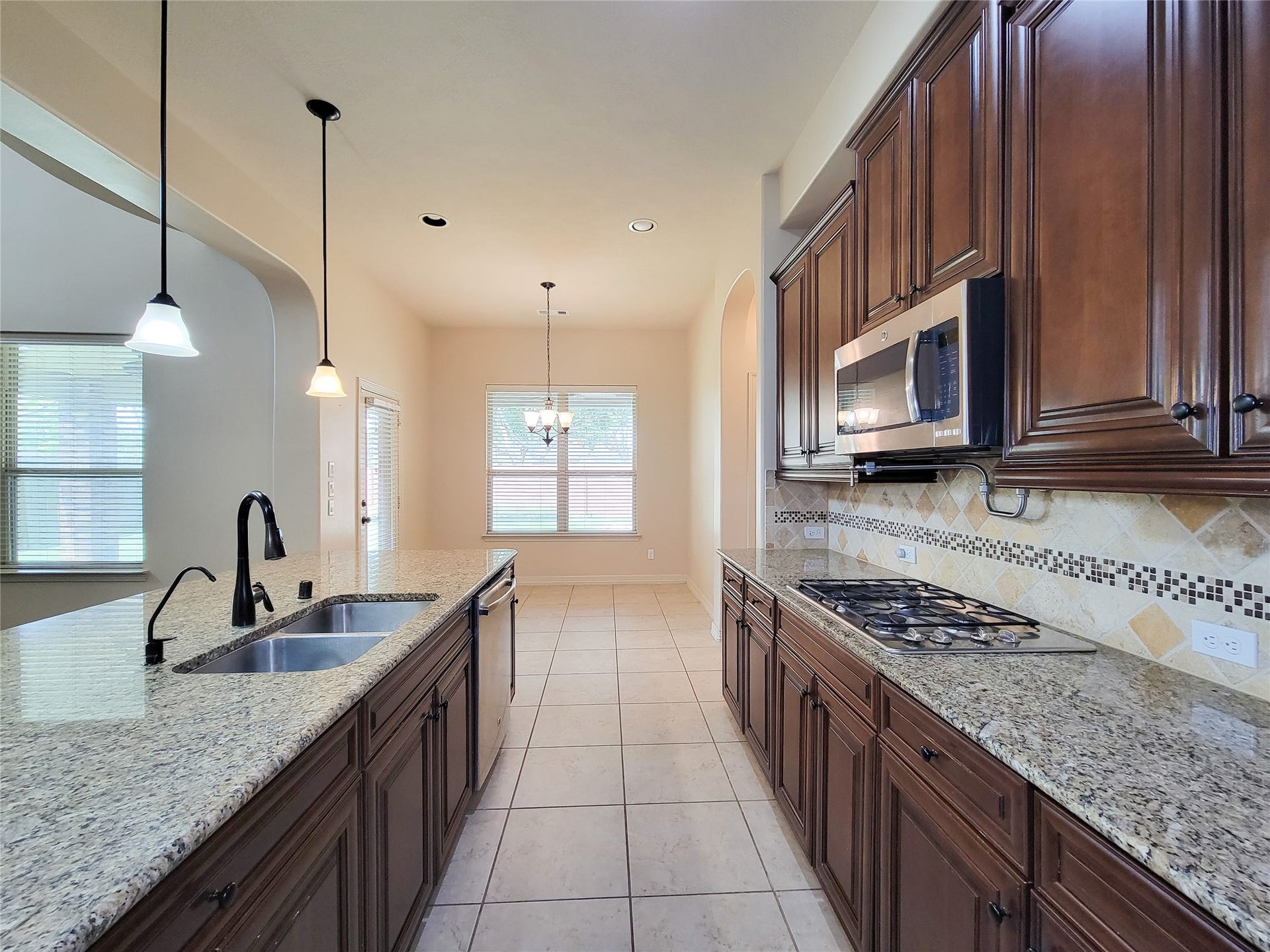 2210 Pearl Bay Court, Pearland, TX 77584 This kitchen features granite countertops, wood cabinetry, and stainless steel appliances. It has a central island with a sink, pendant lighting, and a dining area with large windows for natural light.