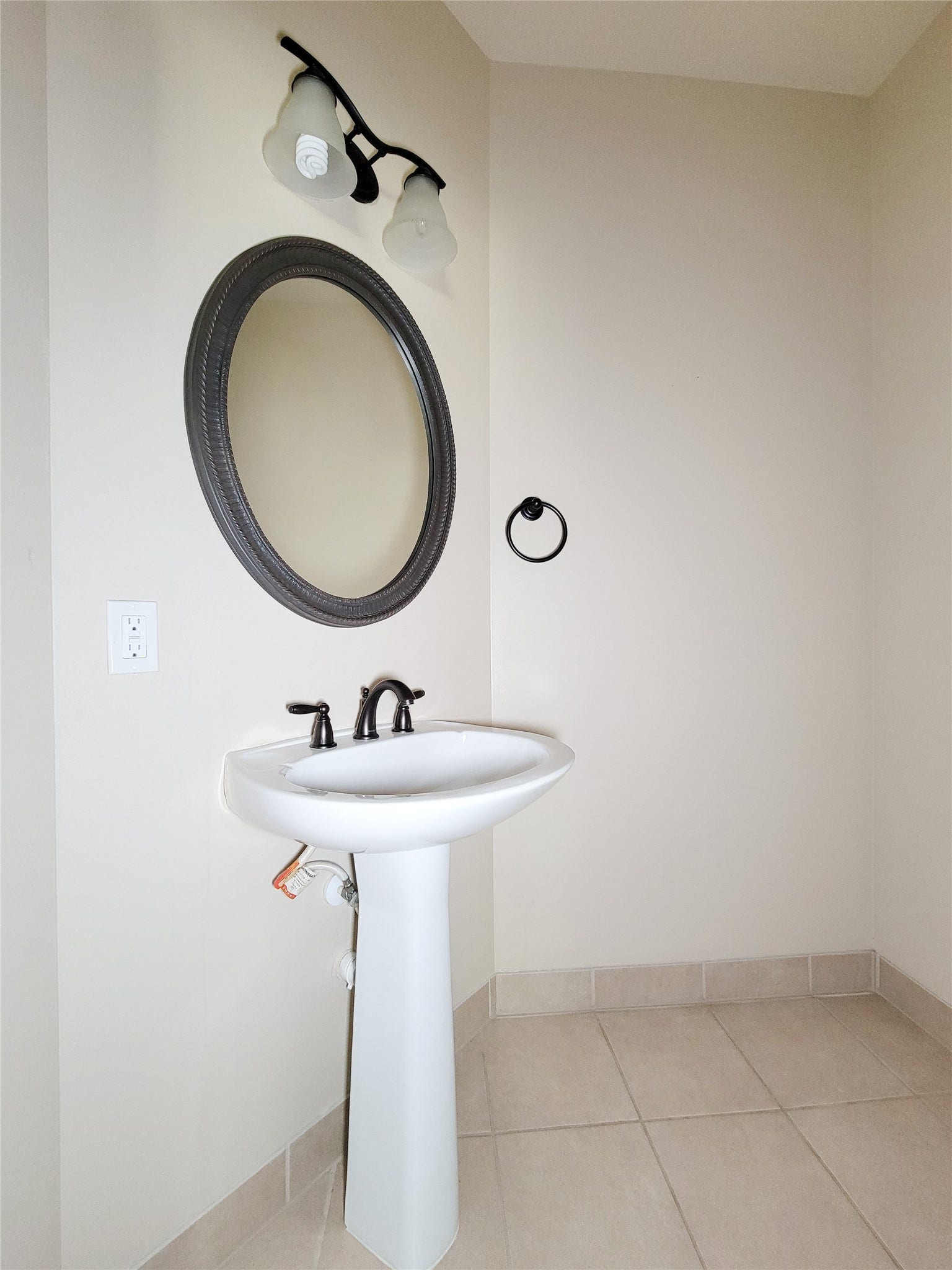 2210 Pearl Bay Court, Pearland, TX 77584 This photo shows a modern, minimalist bathroom with a pedestal sink, circular mirror, and sleek lighting. The neutral tile flooring and wall color create a clean, bright space.