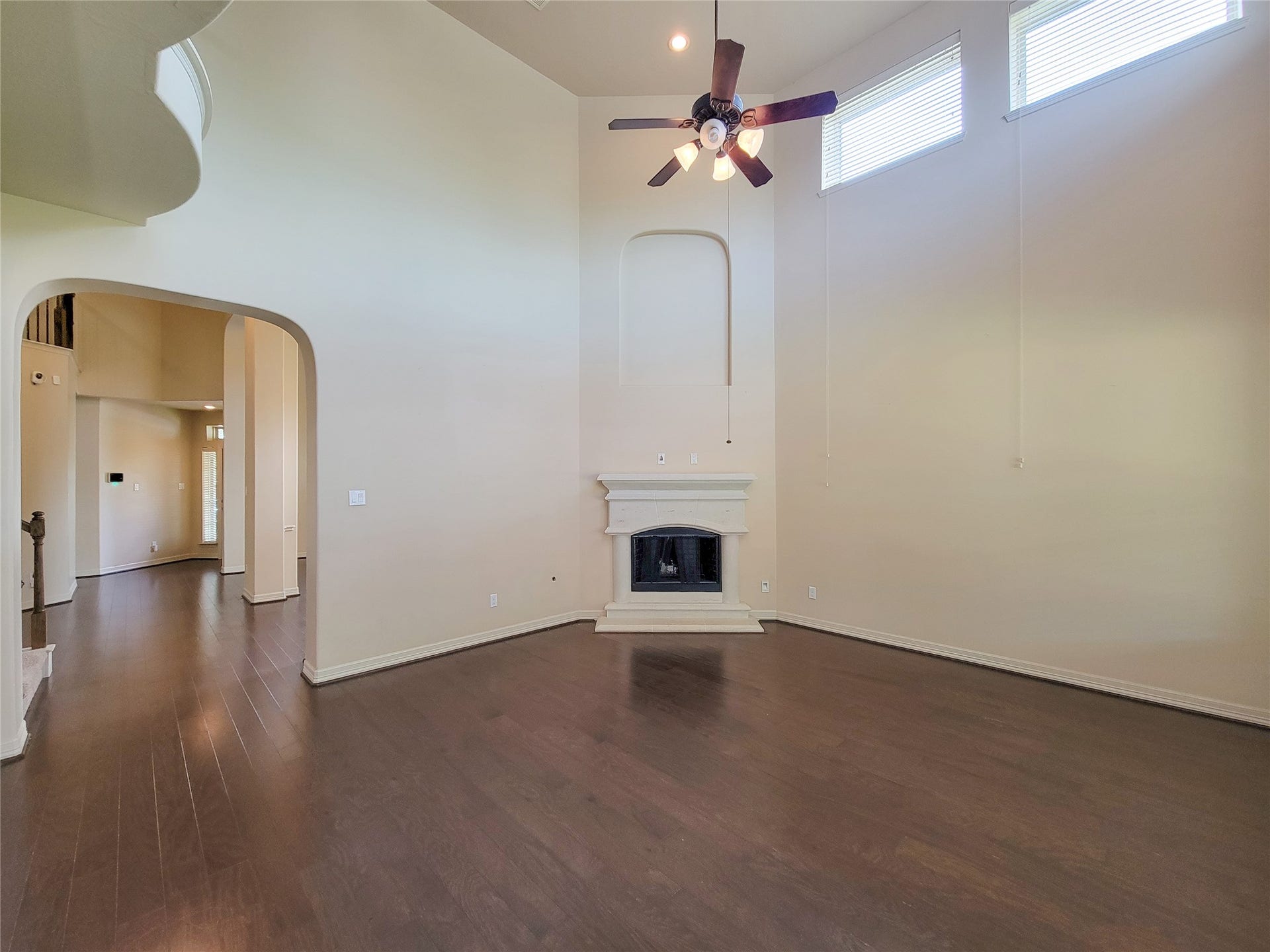 2210 Pearl Bay Court, Pearland, TX 77584 This spacious living room features high ceilings with large windows for natural light, a ceiling fan, hardwood floors, and a central fireplace, creating a bright and inviting atmosphere.
