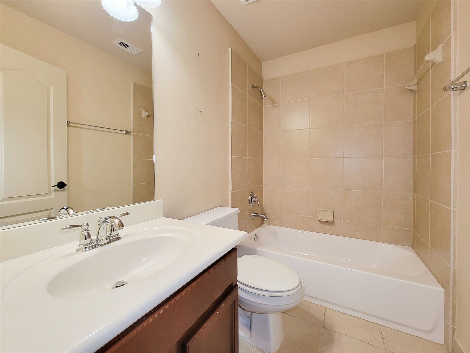 2210 Pearl Bay Court, Pearland, TX 77584 This bathroom features a clean, modern design with a tiled shower and bathtub combo, a sleek white sink with chrome fixtures, and neutral tile flooring, creating a bright and inviting space.
