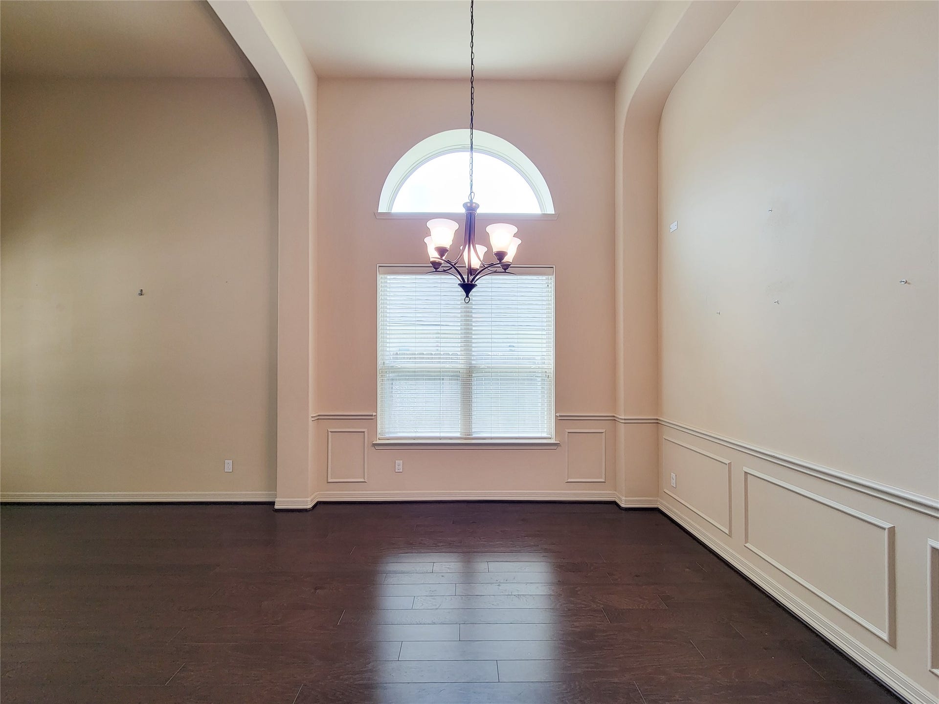 2210 Pearl Bay Court, Pearland, TX 77584 This spacious room features high ceilings, elegant wainscoting, and rich wooden floors. A large window with an arched top allows natural light to fill the space, complemented by a stylish central chandelier. Perfect for a dining or living area.