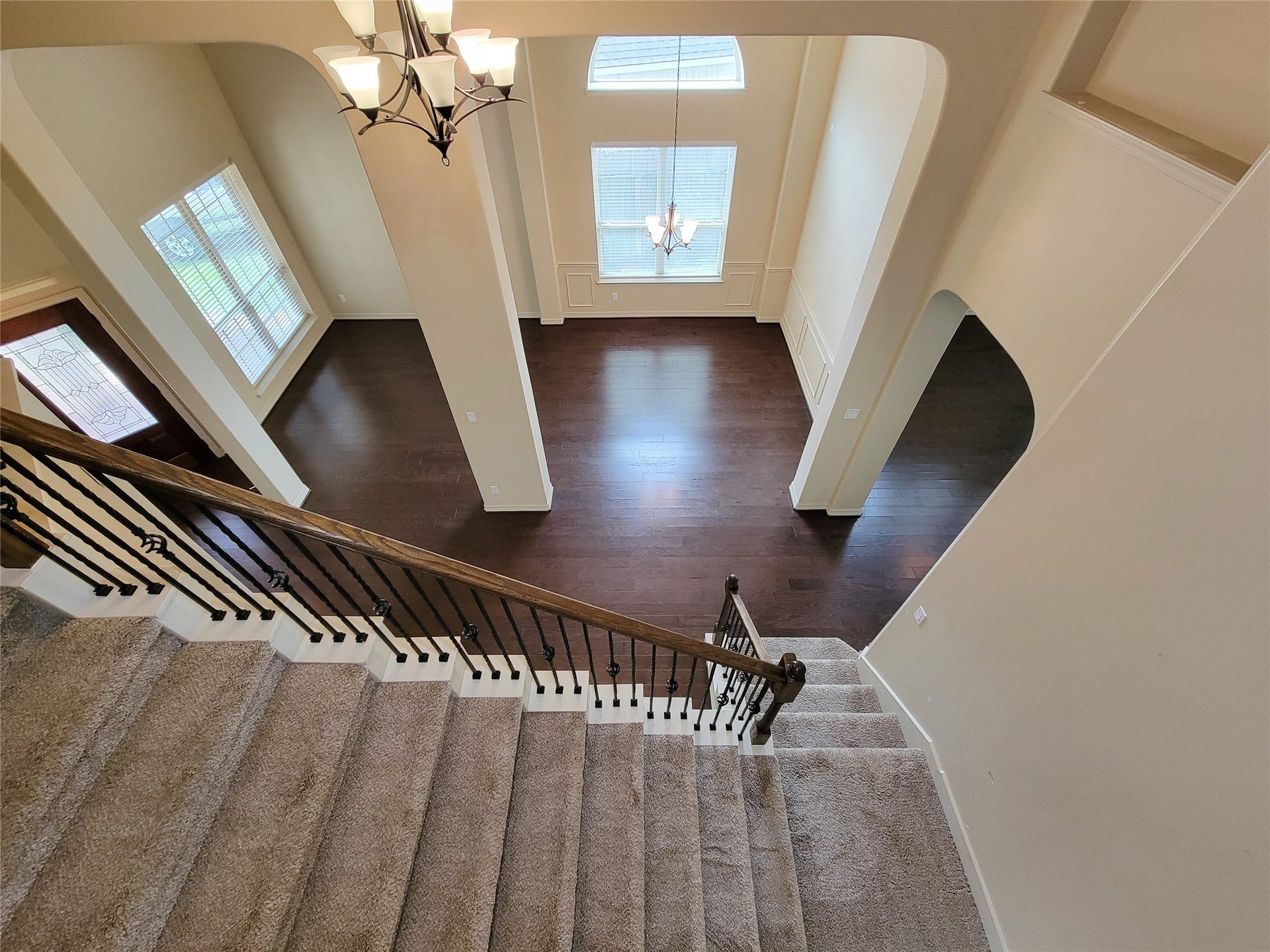 2210 Pearl Bay Court, Pearland, TX 77584 This photo showcases a spacious, open-concept living area with high ceilings and large windows, offering plenty of natural light. It features a charming staircase with carpeted steps and elegant railing, leading to a dark hardwood floor below. A stylish chandelier adds a touch of elegance to the space.