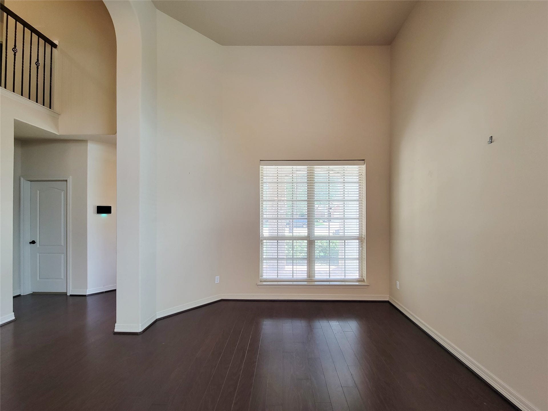 2210 Pearl Bay Court, Pearland, TX 77584 This room features high ceilings and a large window, allowing plenty of natural light. The dark hardwood floors contrast with the light walls, creating a spacious and inviting atmosphere. An elegant railing and doorway add architectural interest.