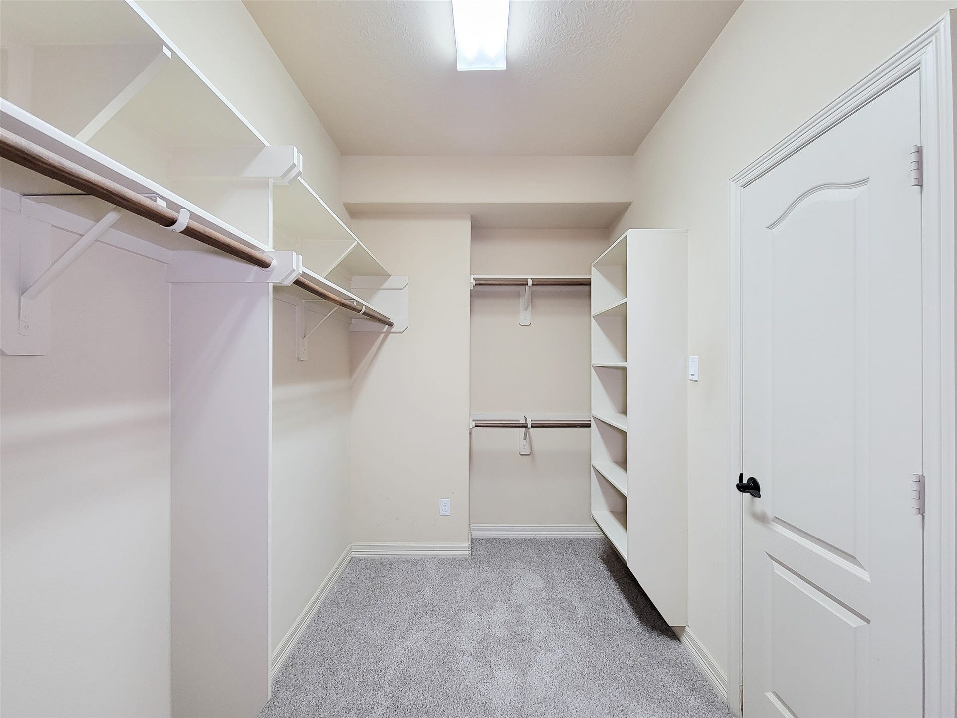 2210 Pearl Bay Court, Pearland, TX 77584 This photo shows a spacious walk-in closet with ample shelving and hanging space, featuring carpeted flooring and a bright overhead light.
