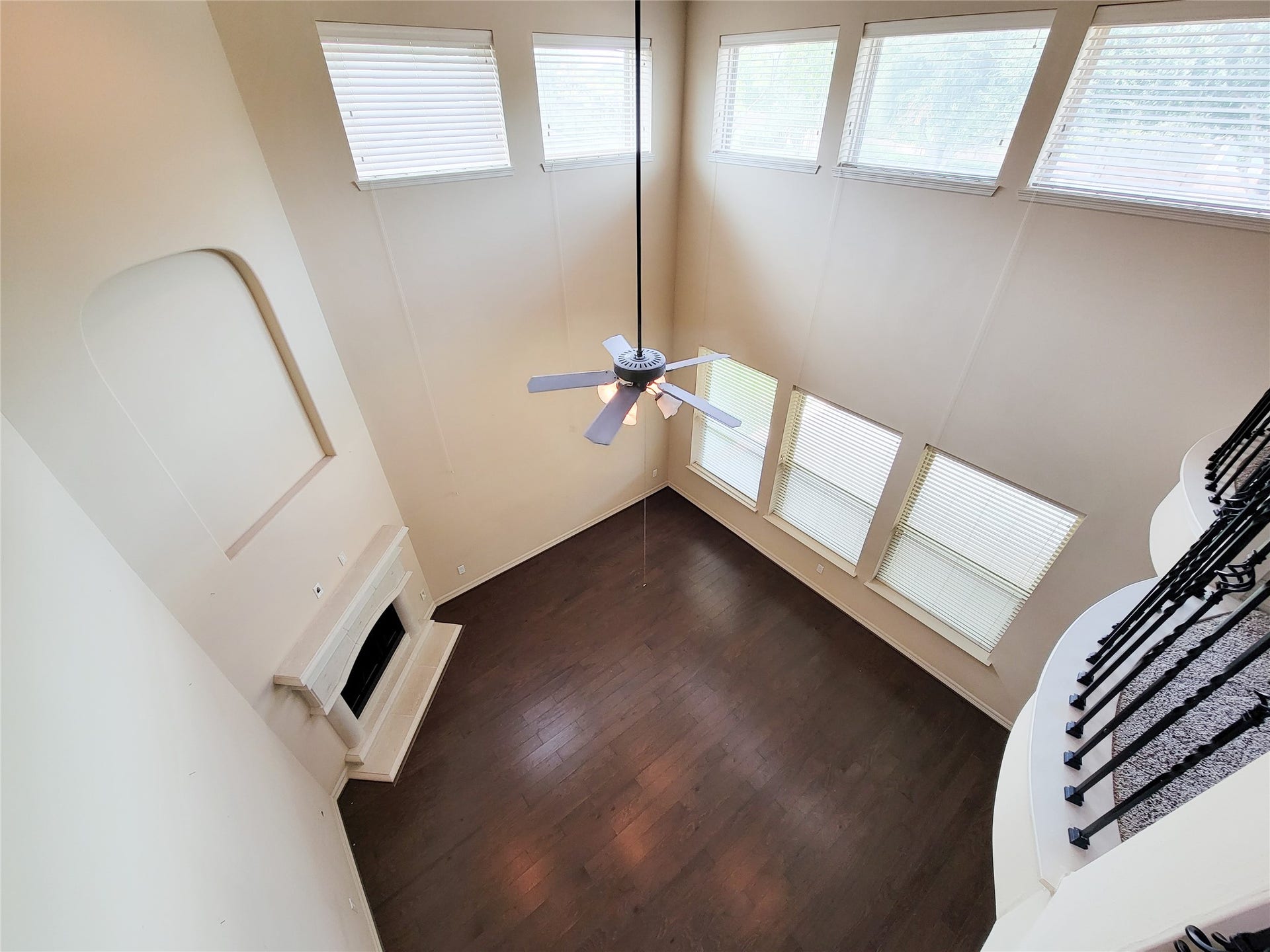 2210 Pearl Bay Court, Pearland, TX 77584 This spacious living room features high ceilings, abundant natural light from large windows, a cozy fireplace, and elegant dark wood flooring. A ceiling fan adds comfort, while an open staircase provides a stylish touch.