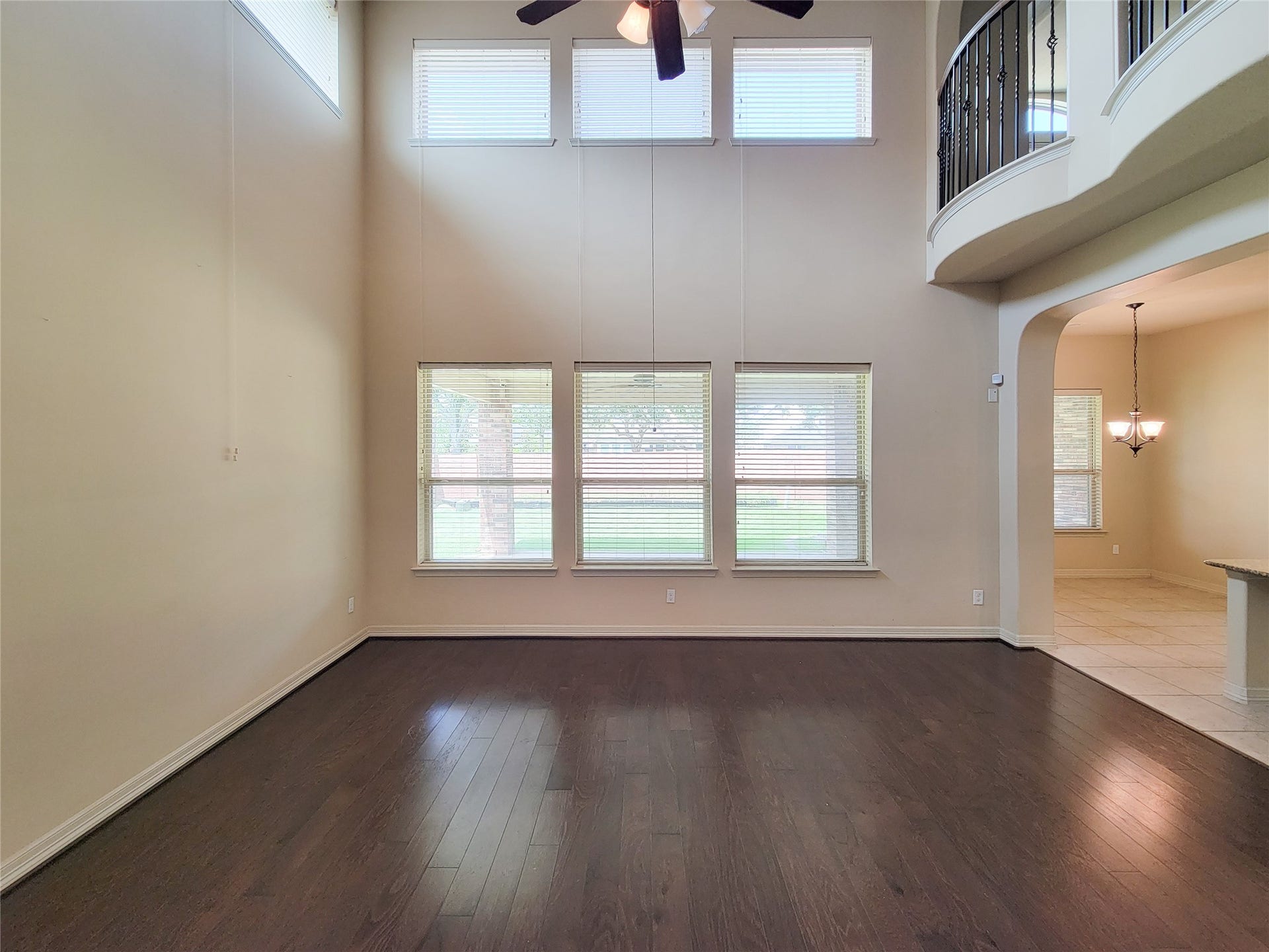 2210 Pearl Bay Court, Pearland, TX 77584 This spacious living area features high ceilings, abundant natural light from large windows, elegant dark hardwood flooring, and an open balcony. It seamlessly connects to a tiled dining area with a stylish chandelier, creating an inviting and airy atmosphere.
