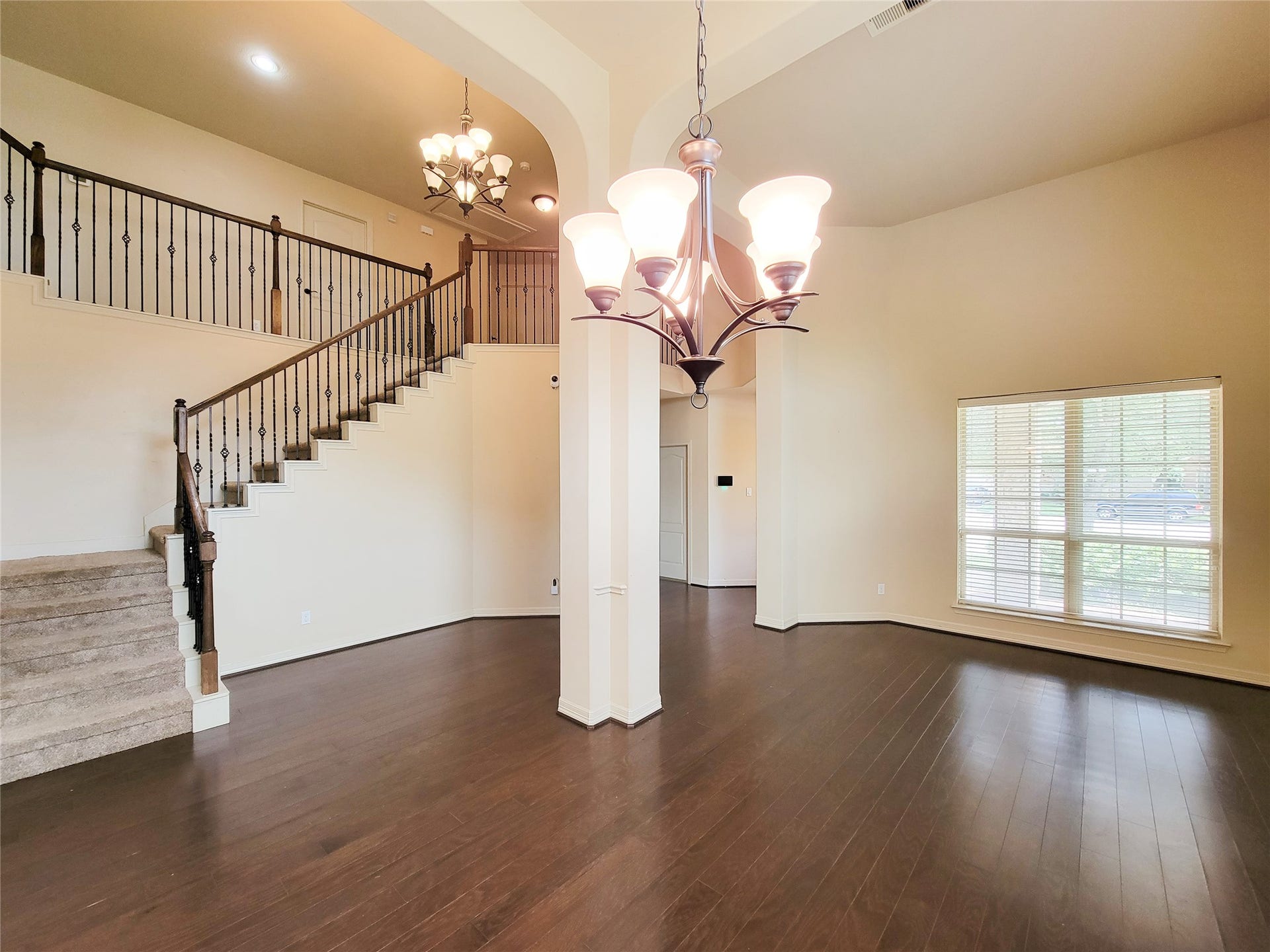2210 Pearl Bay Court, Pearland, TX 77584 This spacious living area features high ceilings, elegant wood flooring, and a modern chandelier. It includes a staircase with wrought iron railings, a large window for natural light, and a neutral color palette, creating a warm and inviting atmosphere.