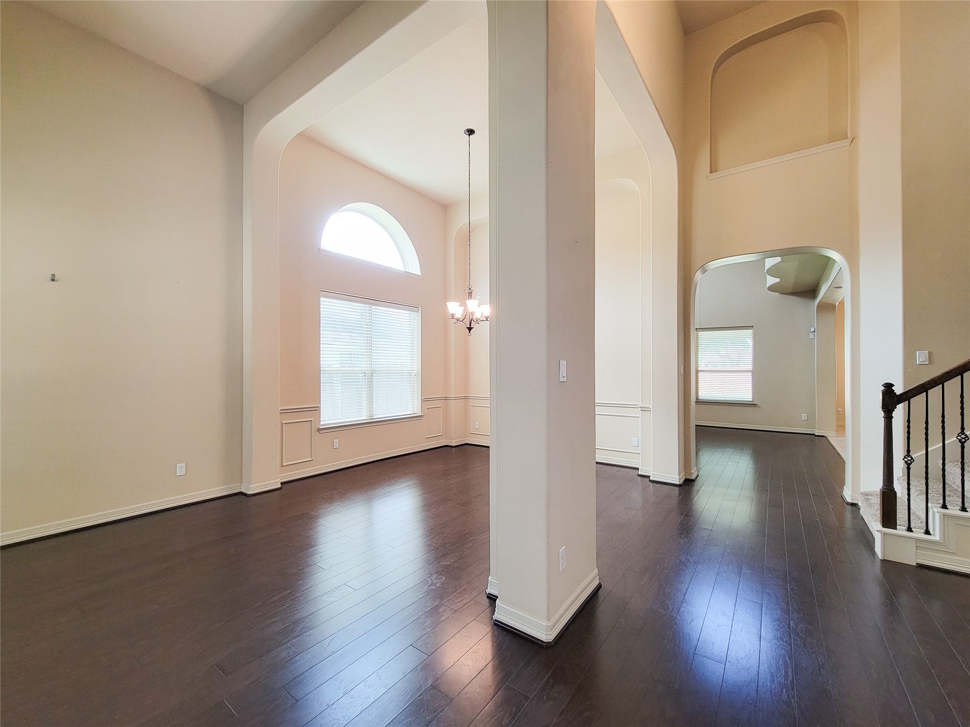 2210 Pearl Bay Court, Pearland, TX 77584 This spacious home interior features high ceilings, large windows for natural light, and elegant dark wood flooring. The open layout includes a dining area with a chandelier, leading into a separate living space, adding to the airy, welcoming ambiance.