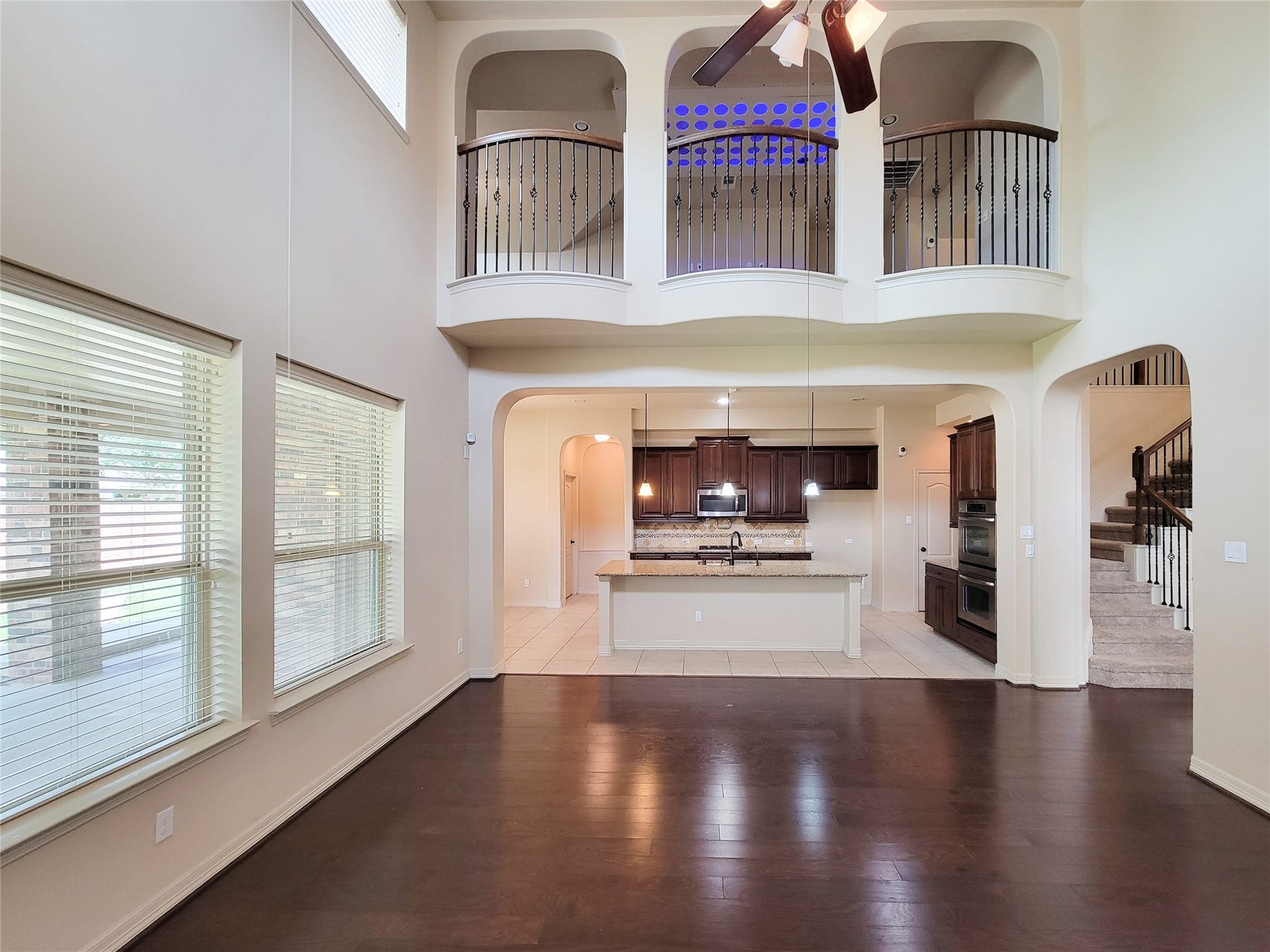 2210 Pearl Bay Court, Pearland, TX 77584 This spacious open-concept living area features high ceilings, large windows for natural light, and elegant dark wood flooring. The kitchen boasts modern appliances, a large island, and stylish cabinetry. An intricate railing balcony overlooks the space, adding a touch of sophistication.