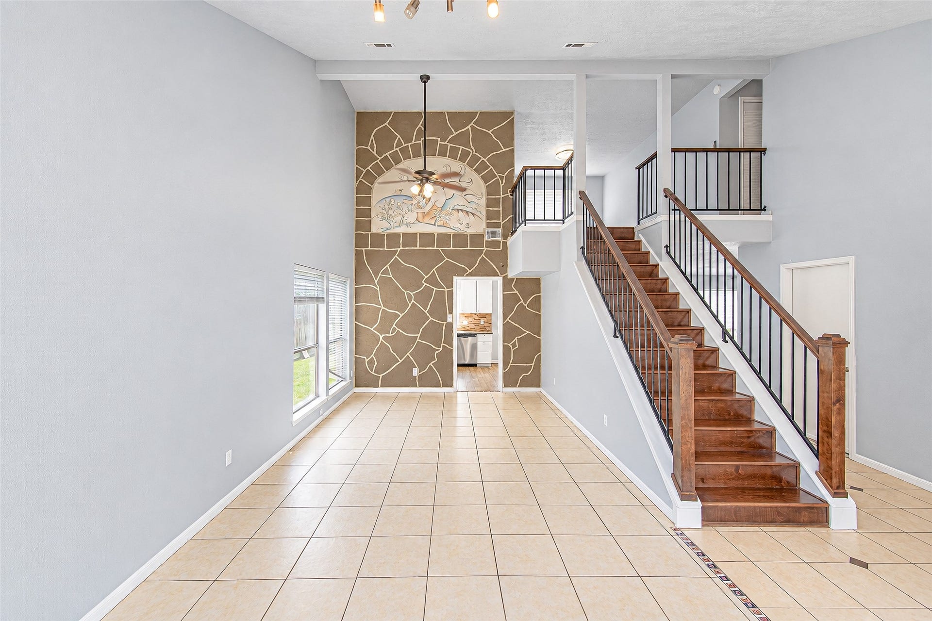 12027 Huntington Park Drive, Houston, TX 77099 Spacious open living area with elegant tile flooring, a striking stone accent wall, and a grand staircase leading to the upper level, exuding warmth and style.