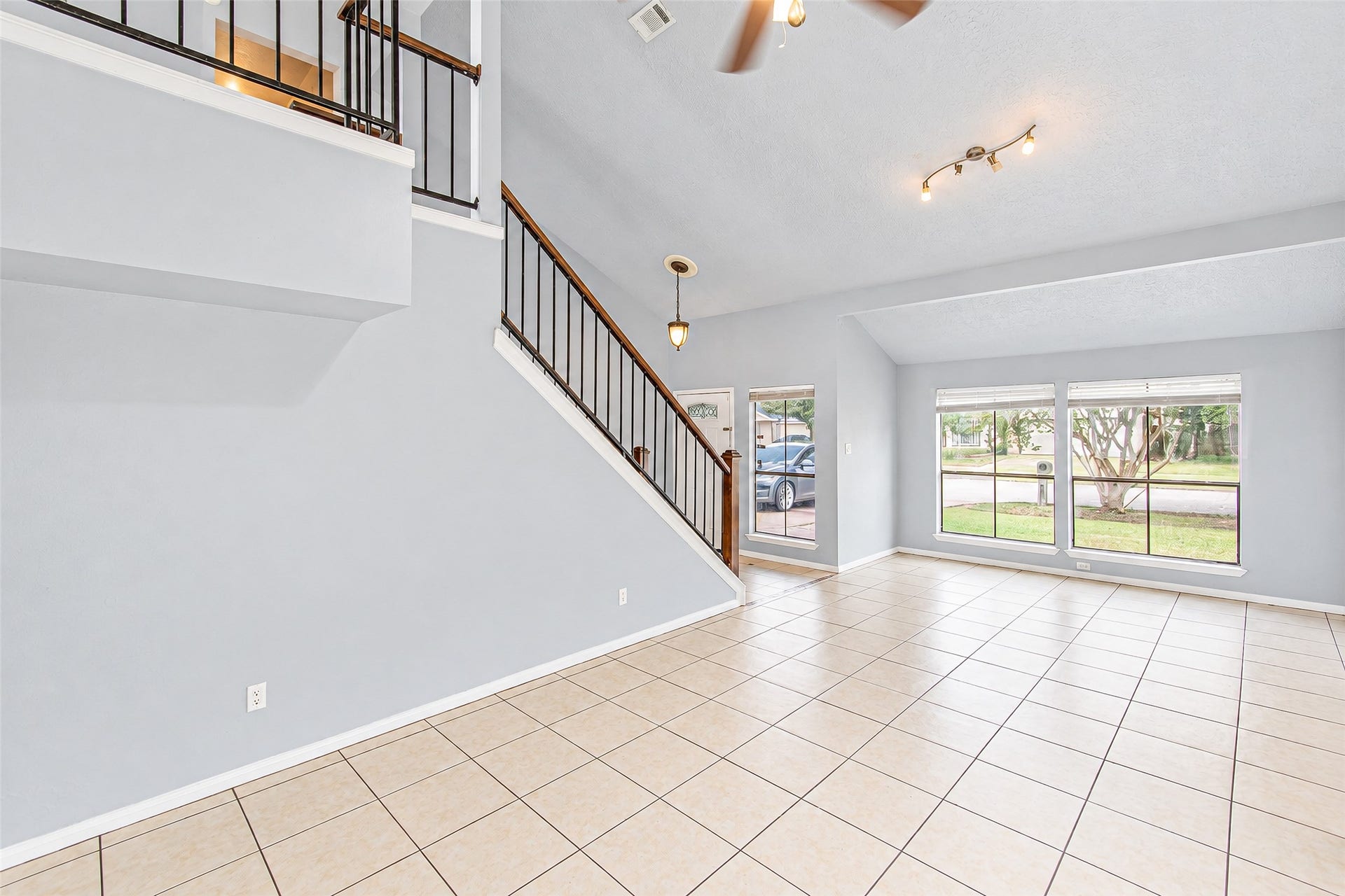 12027 Huntington Park Drive, Houston, TX 77099 Spacious living area with high ceilings and large windows offering abundant natural light, complemented by a modern staircase and tiled flooring.