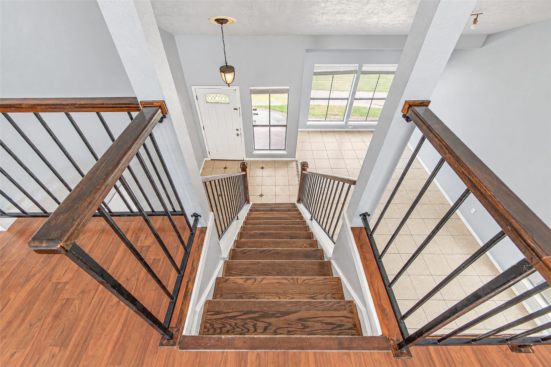 12027 Huntington Park Drive, Houston, TX 77099 Elegant staircase with rich wood steps and sleek black railings leads to a bright foyer with large windows and tile flooring.