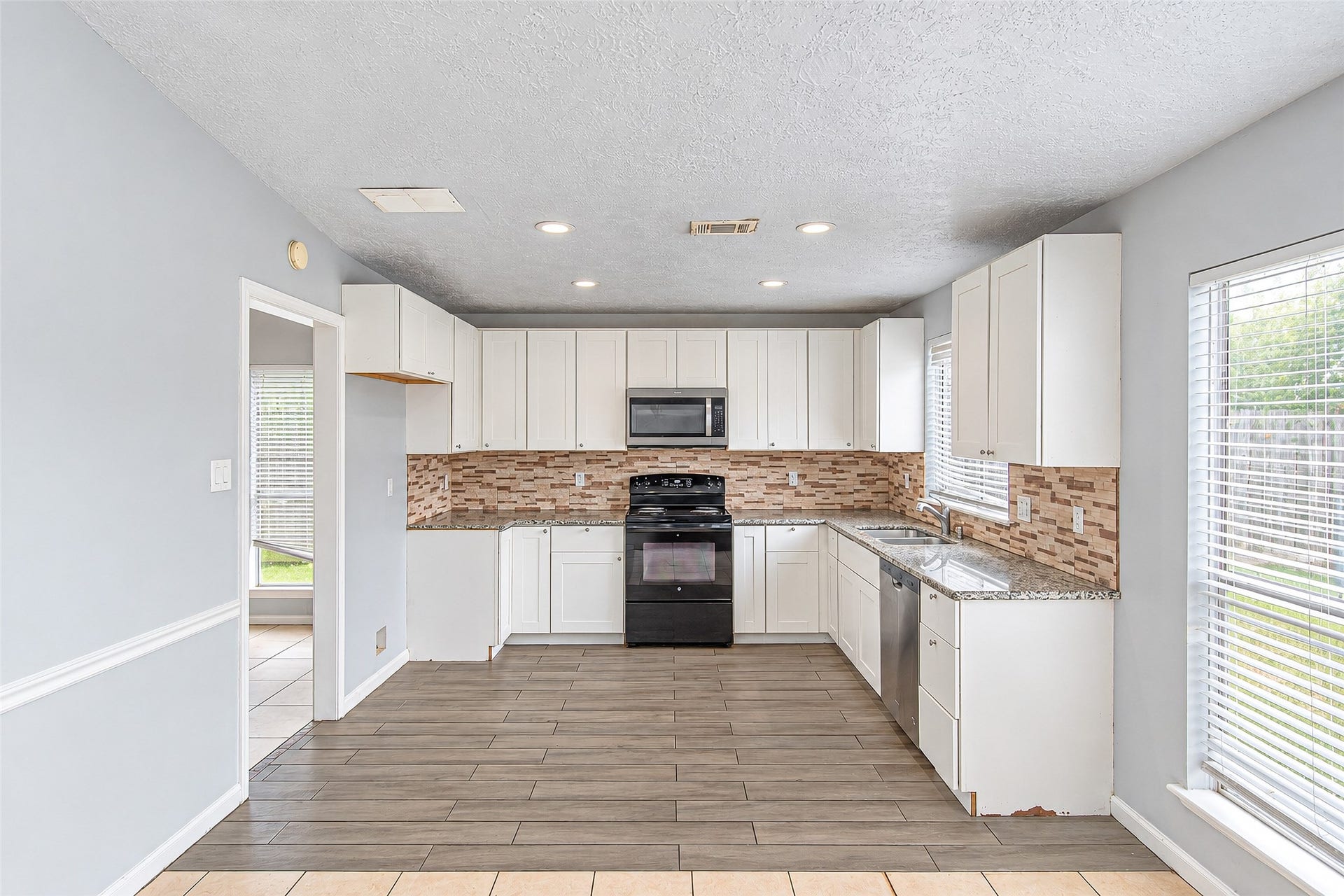 12027 Huntington Park Drive, Houston, TX 77099 Bright and modern kitchen featuring sleek white cabinetry, granite countertops, and a stylish tile backsplash, with ample natural light streaming through large windows.