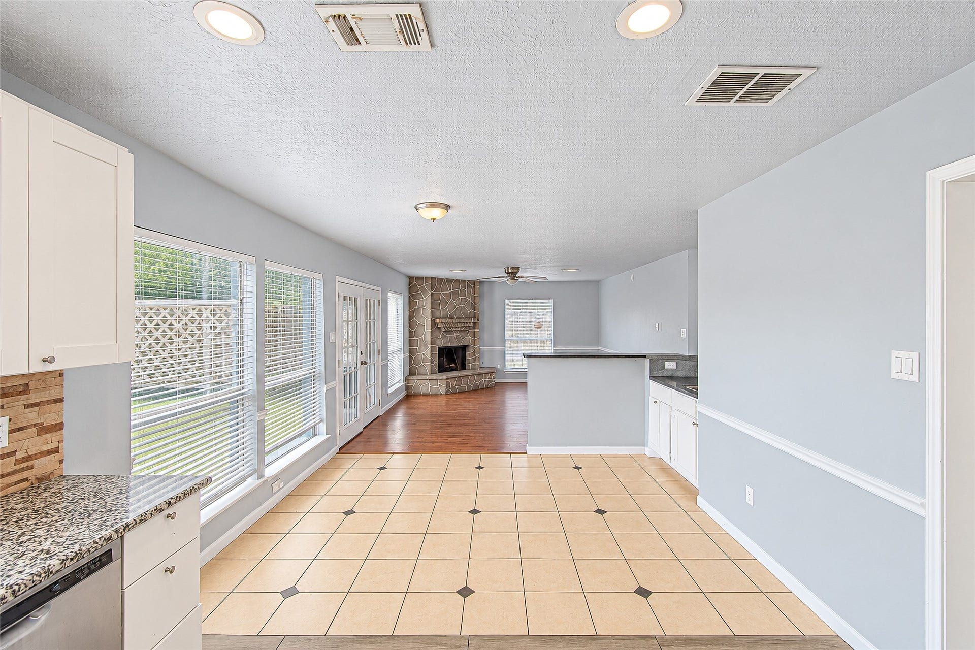 12027 Huntington Park Drive, Houston, TX 77099 Bright and open living space with large windows, featuring a cozy stone fireplace and a seamless transition from tiled kitchen to hardwood floors.