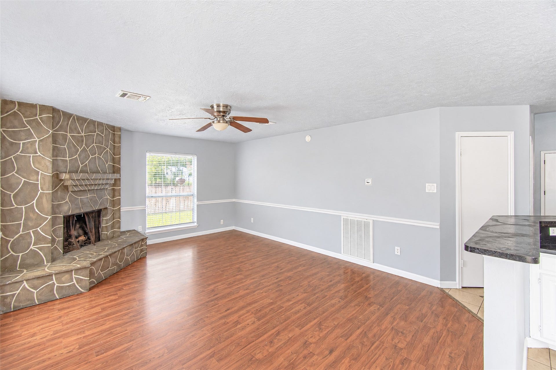 12027 Huntington Park Drive, Houston, TX 77099 Spacious living area with elegant wood flooring and a unique stone fireplace, complemented by soft gray walls and ample natural light.