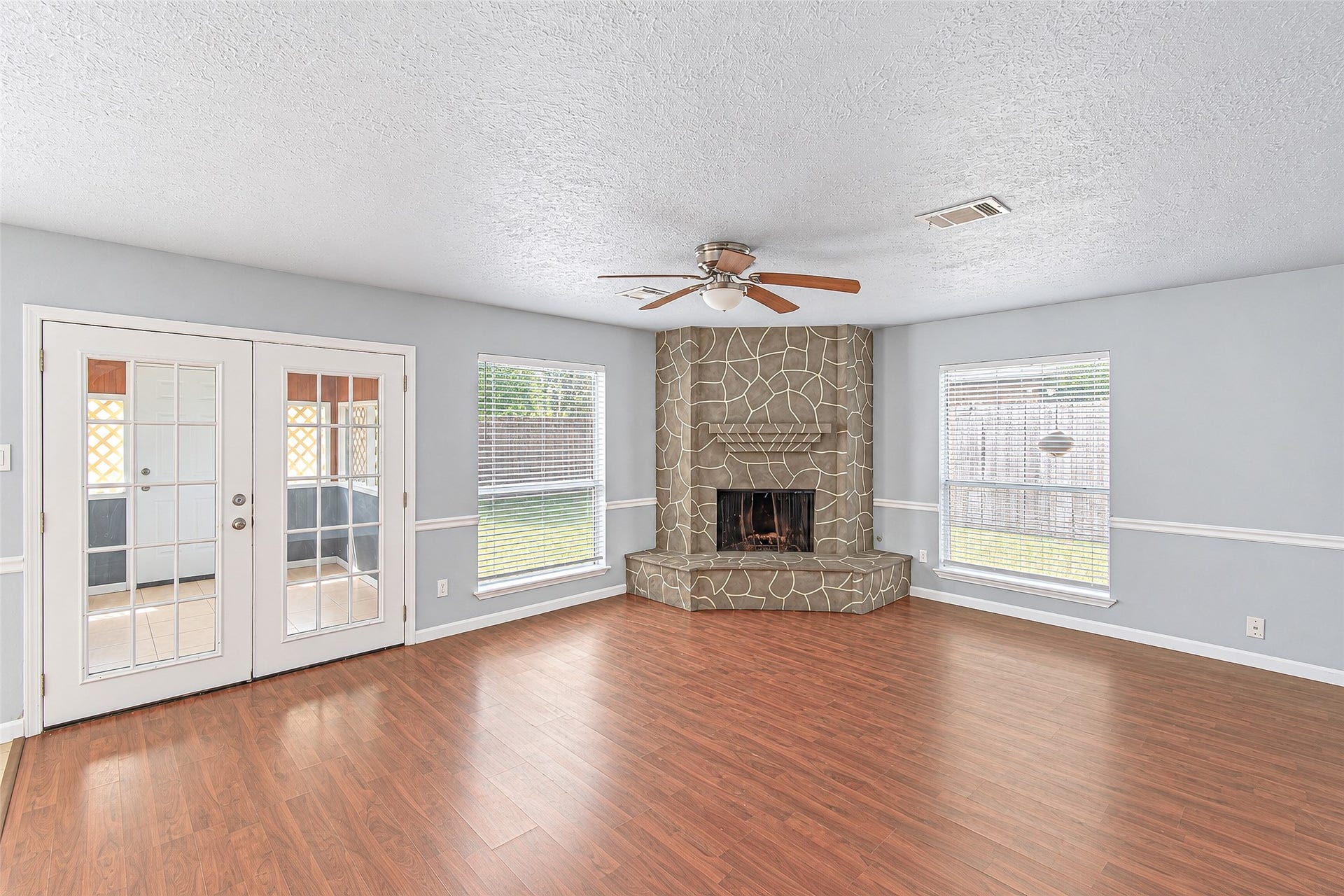 12027 Huntington Park Drive, Houston, TX 77099 Spacious living room with elegant wood flooring, a striking stone fireplace, and abundant natural light from large windows and French doors.