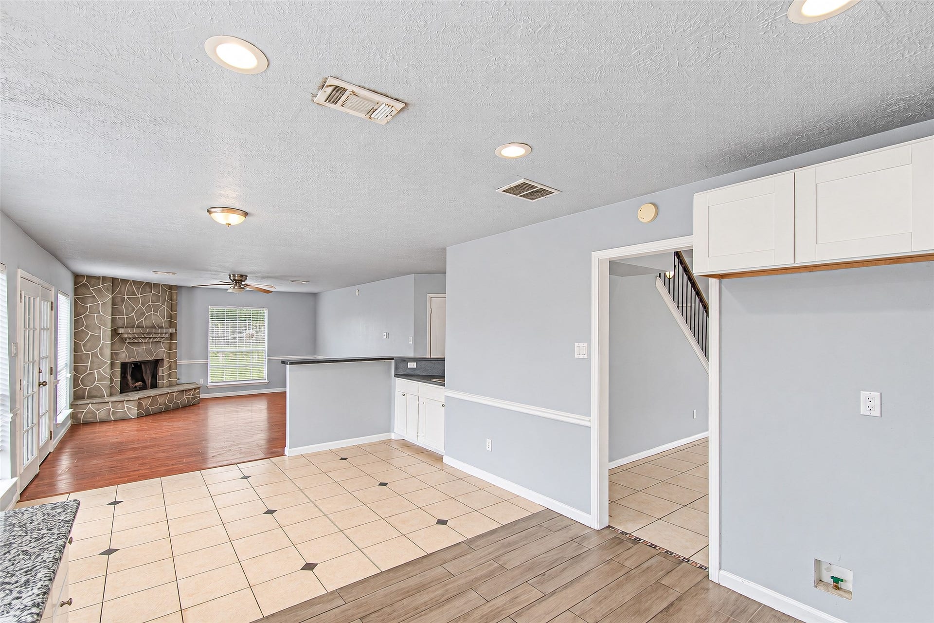 12027 Huntington Park Drive, Houston, TX 77099 Bright and spacious open-concept living area featuring a cozy stone fireplace, tile and wood flooring, and ample natural light from large windows and French doors.